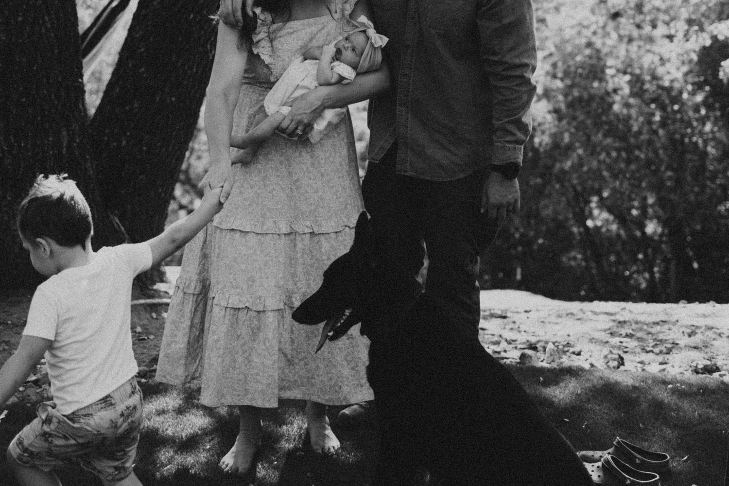 Black and white photo of family with young child and newborn outdoors.