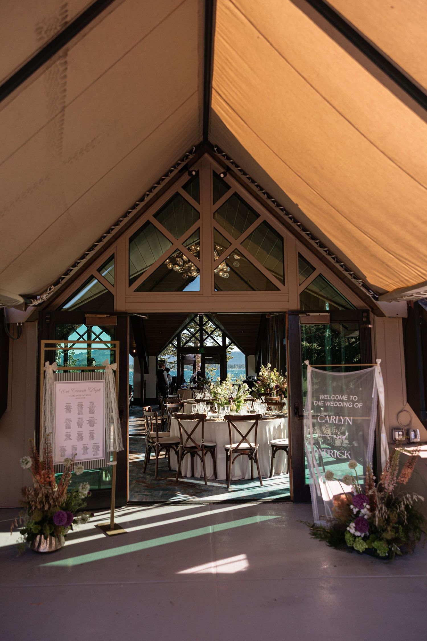 Elegant wedding reception tent venue with wooden doors open revealing floral centerpieces, dining tables, and welcome signage.