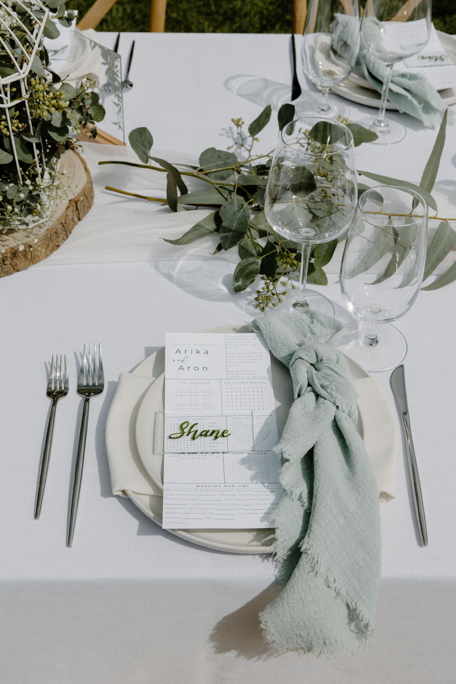 Elegant wedding table setting with sage green napkin, eucalyptus greenery, and personalized place card.