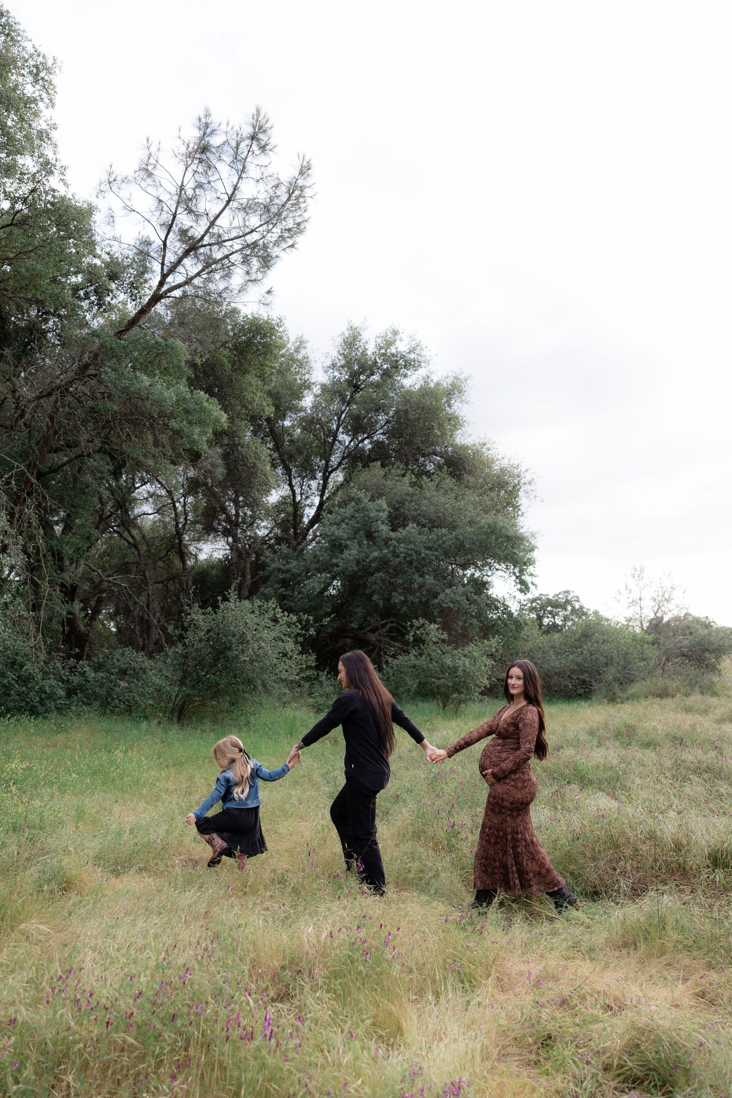 Two women and a young girl holding hands while walking through a wildflower meadow.