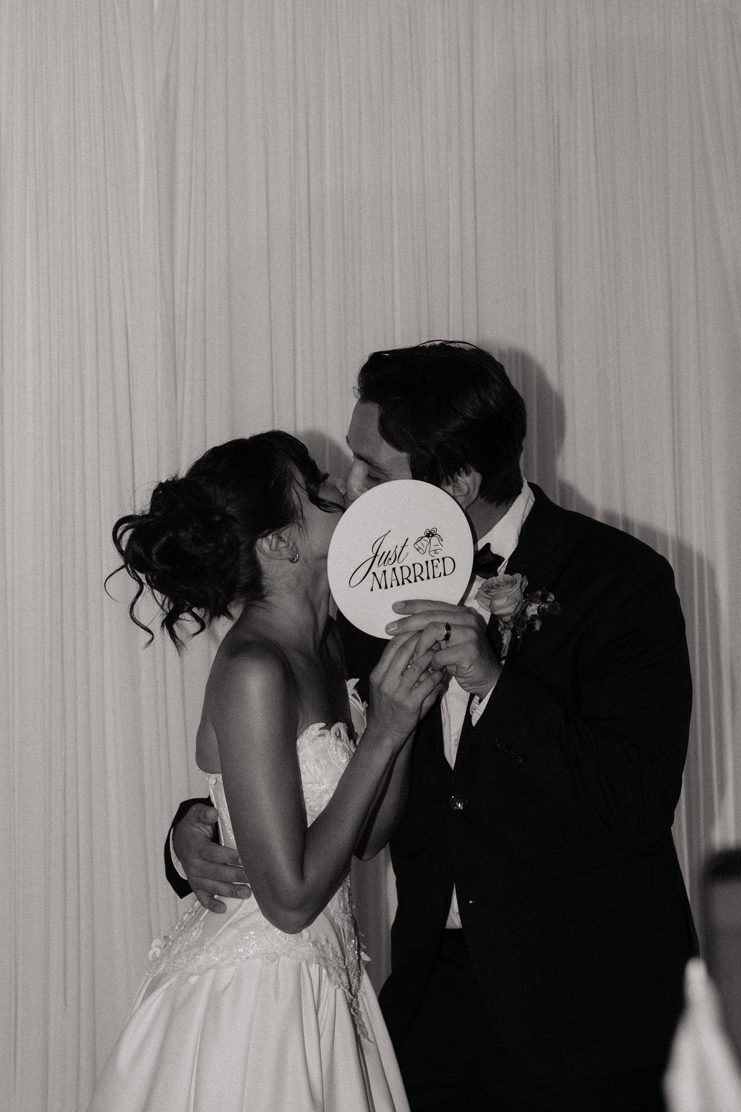 Bride and groom kissing behind a Just Married sign at their wedding reception in black and white.