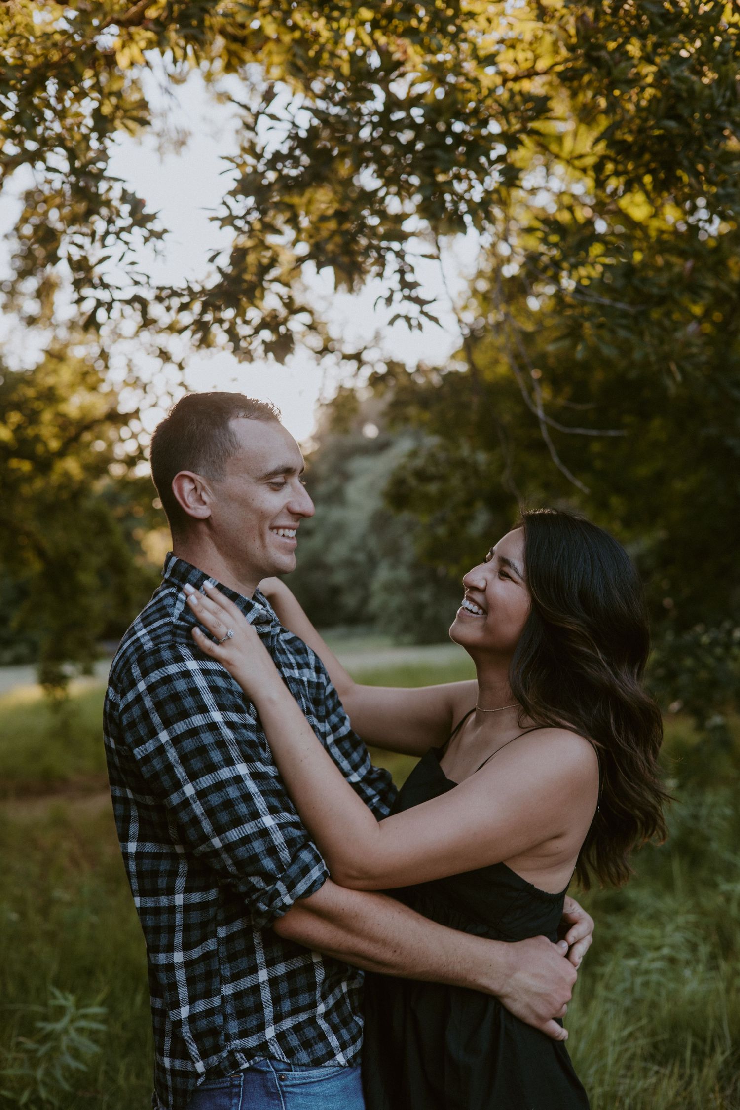 Happy couple embracing and laughing under golden sunlit trees in a green park.