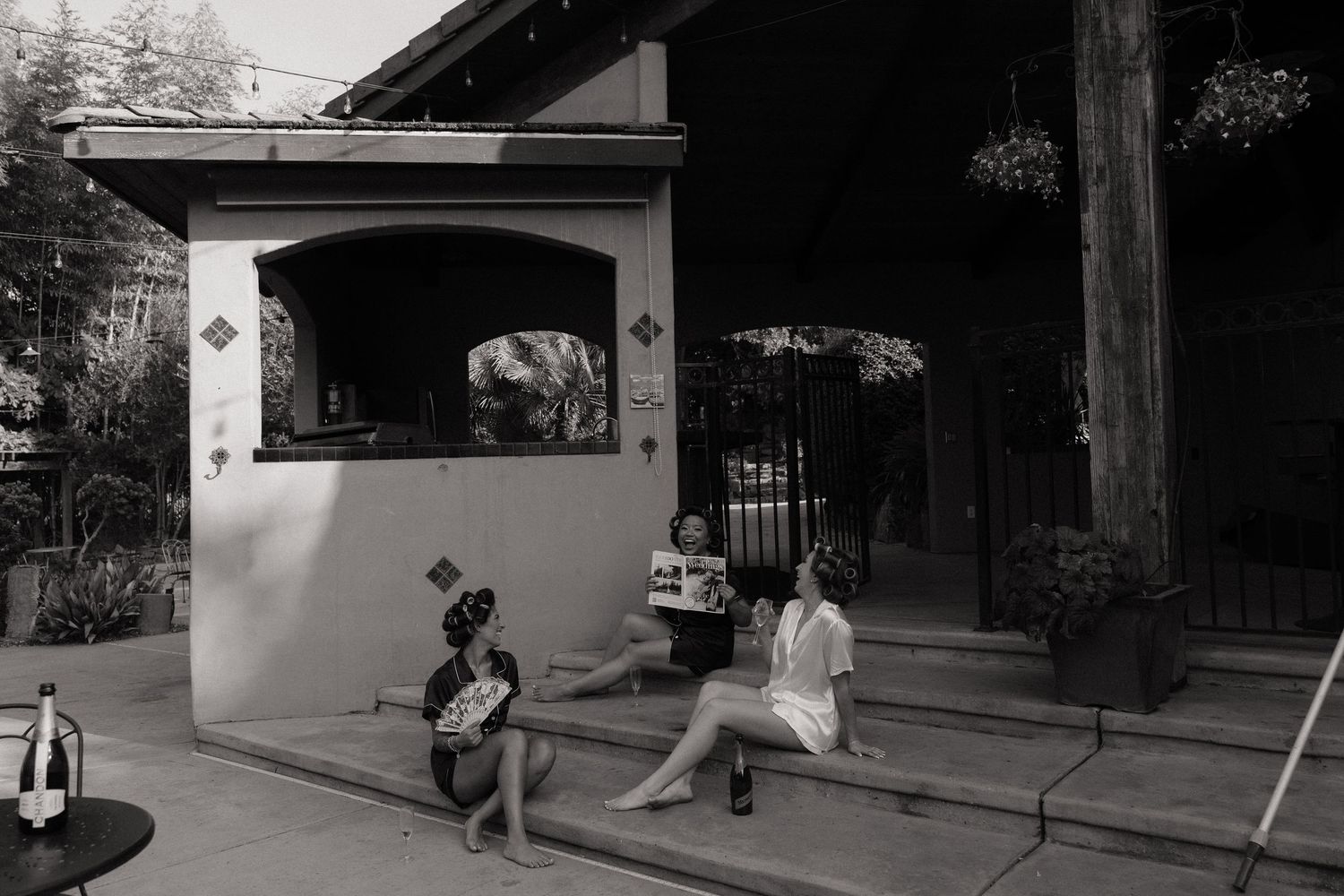 Black and white photo of people relaxing on steps outside a rustic building with lush greenery.