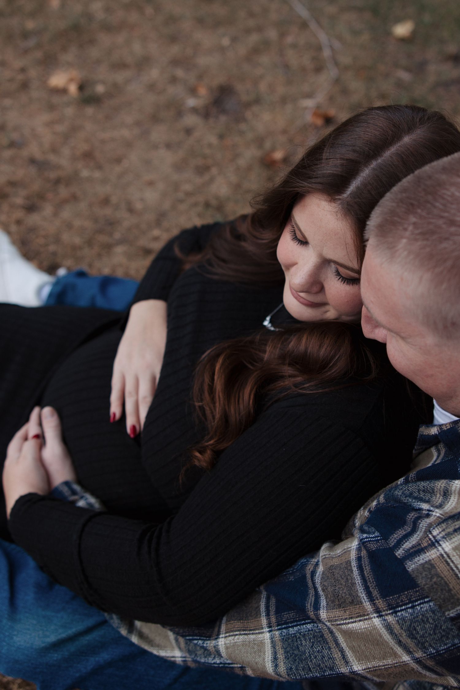 Couple cuddles closely on a blanket outdoors in an intimate fall engagement photo session.