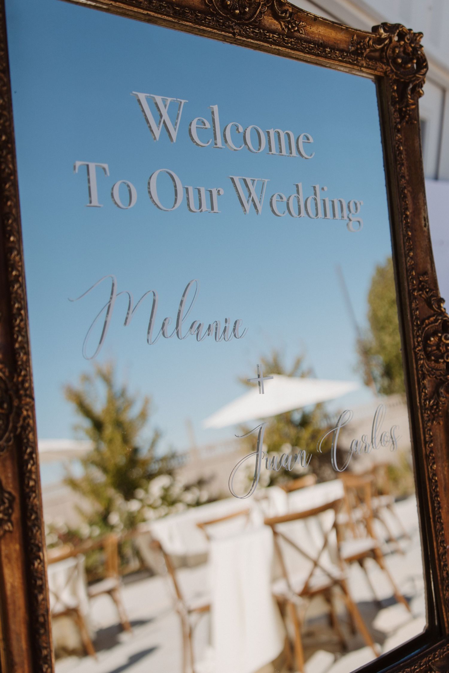 Elegant gold-framed mirror welcome sign reading Welcome To Our Wedding Melanie and Juan Carlos.