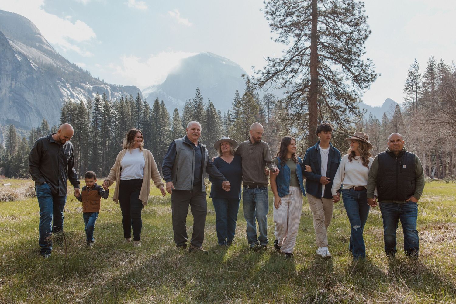 An extended family walks together hand-in-hand through a meadow with stunning mountain views in Yosemite.