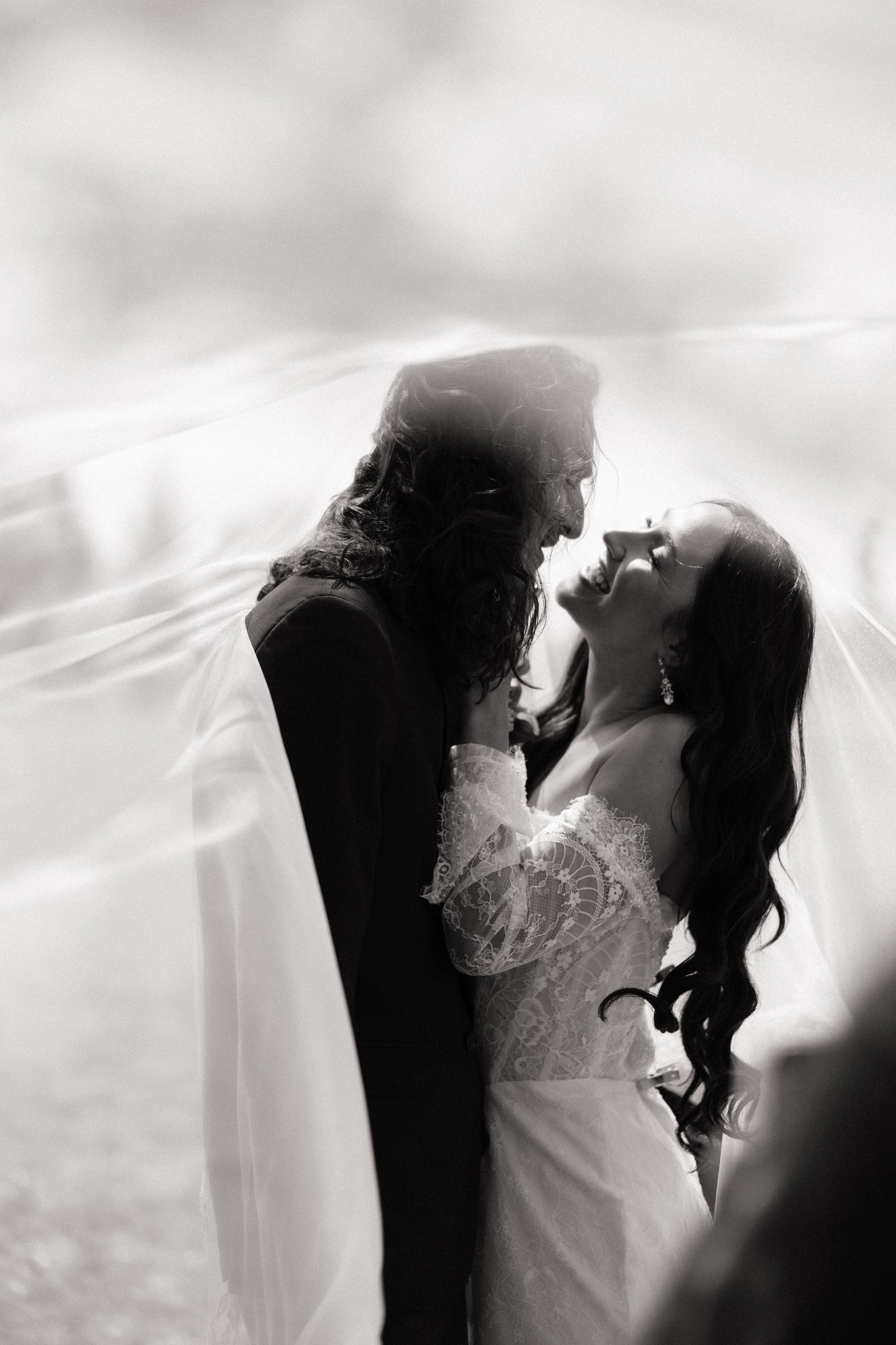 Bride and groom sharing an intimate romantic moment under a flowing veil at their wedding.