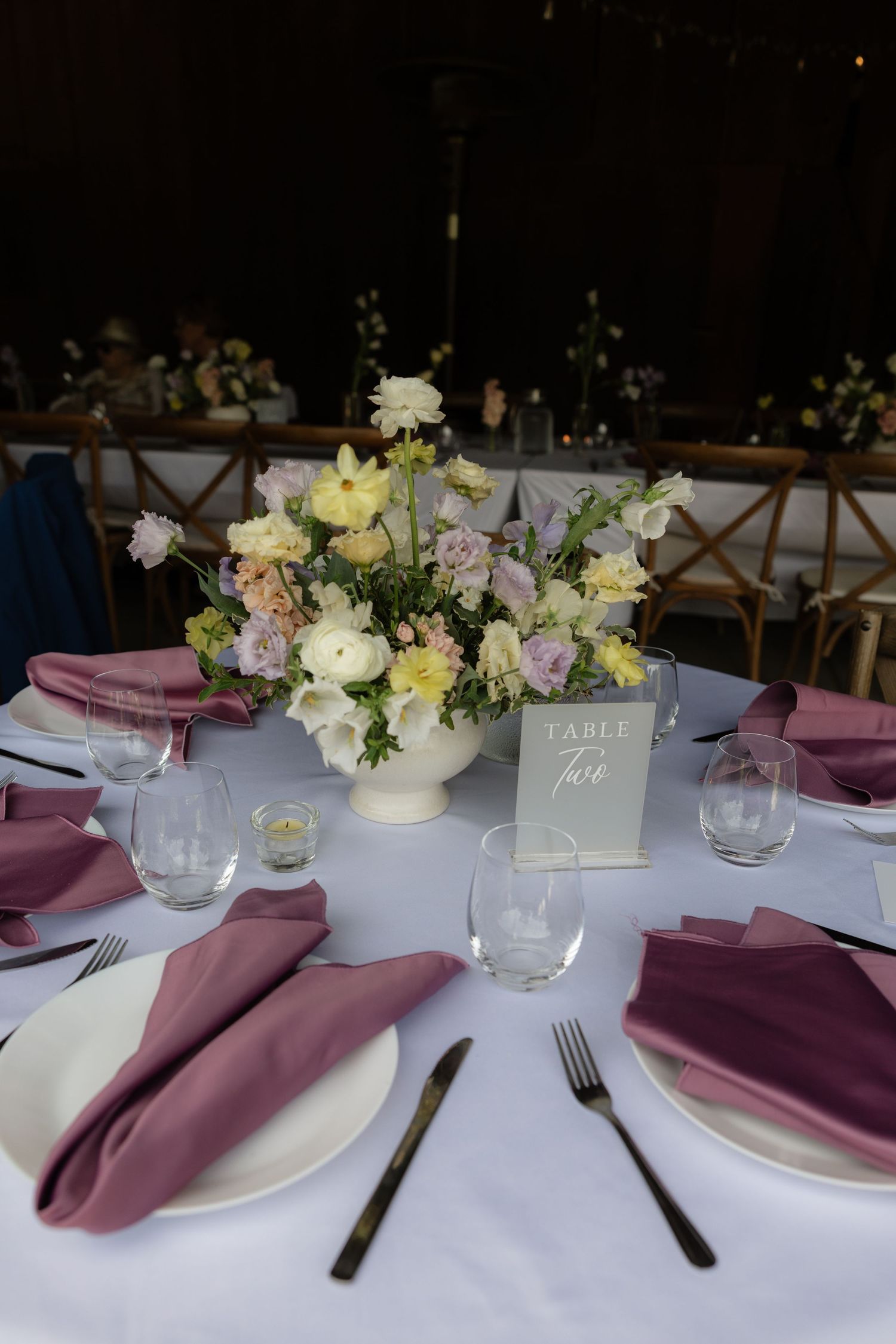 Wedding reception table set with dusty rose napkins, white floral centerpiece, and a table five card on white linen.