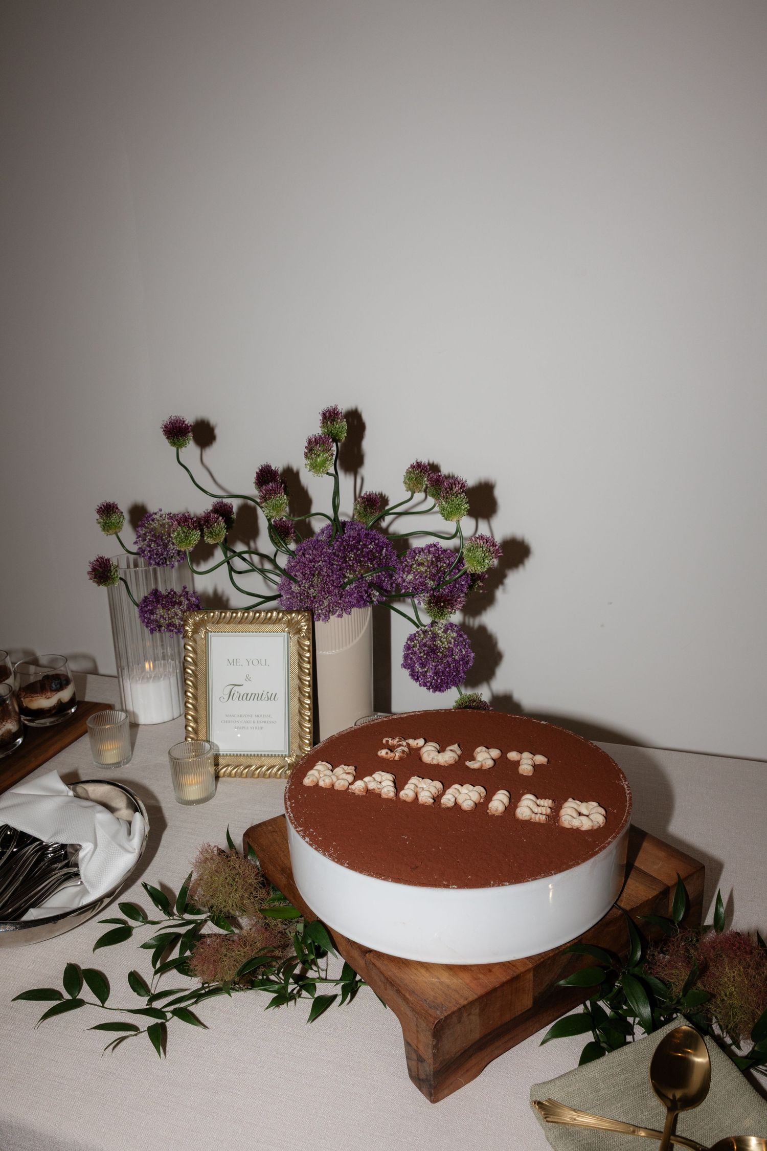 A chocolate wedding cake reading Just Married on a wooden stand, surrounded by purple flowers and greenery.