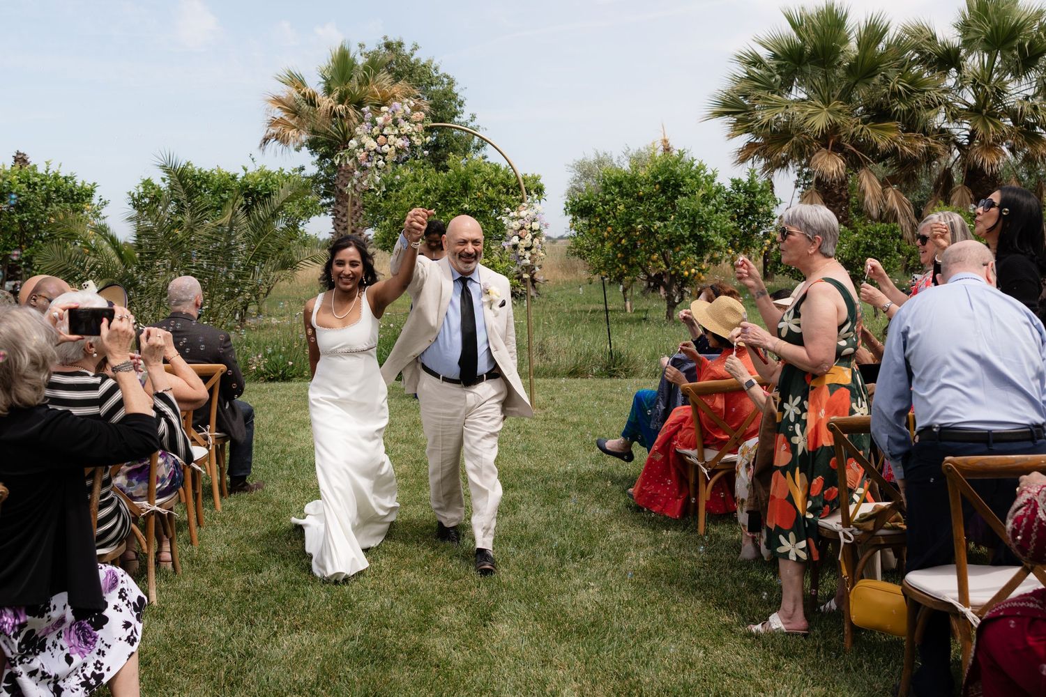 Newlyweds celebrate joyfully as they walk down the aisle at their outdoor garden wedding ceremony.