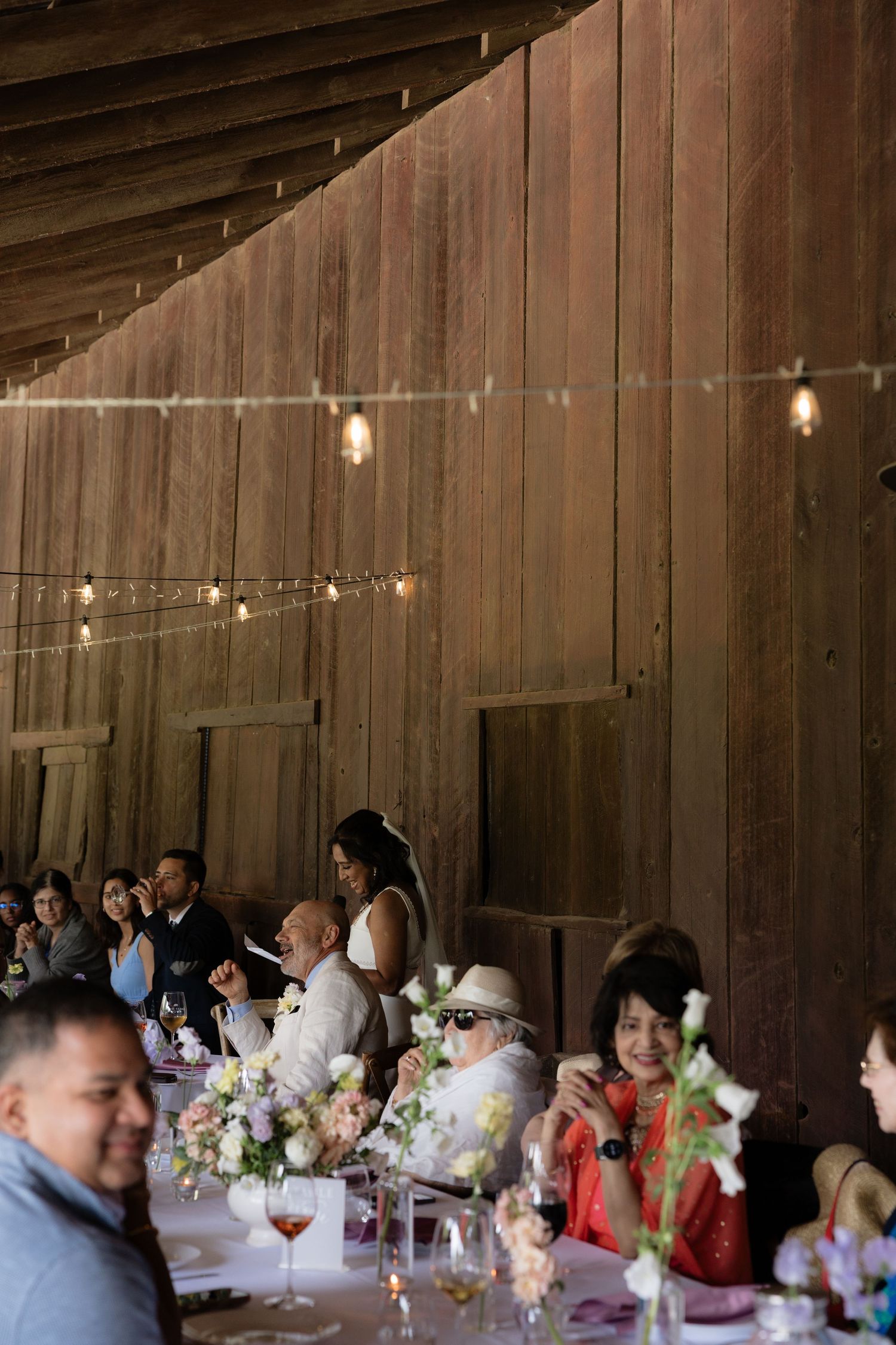 Wedding guests seated at decorated tables inside rustic barn venue.
