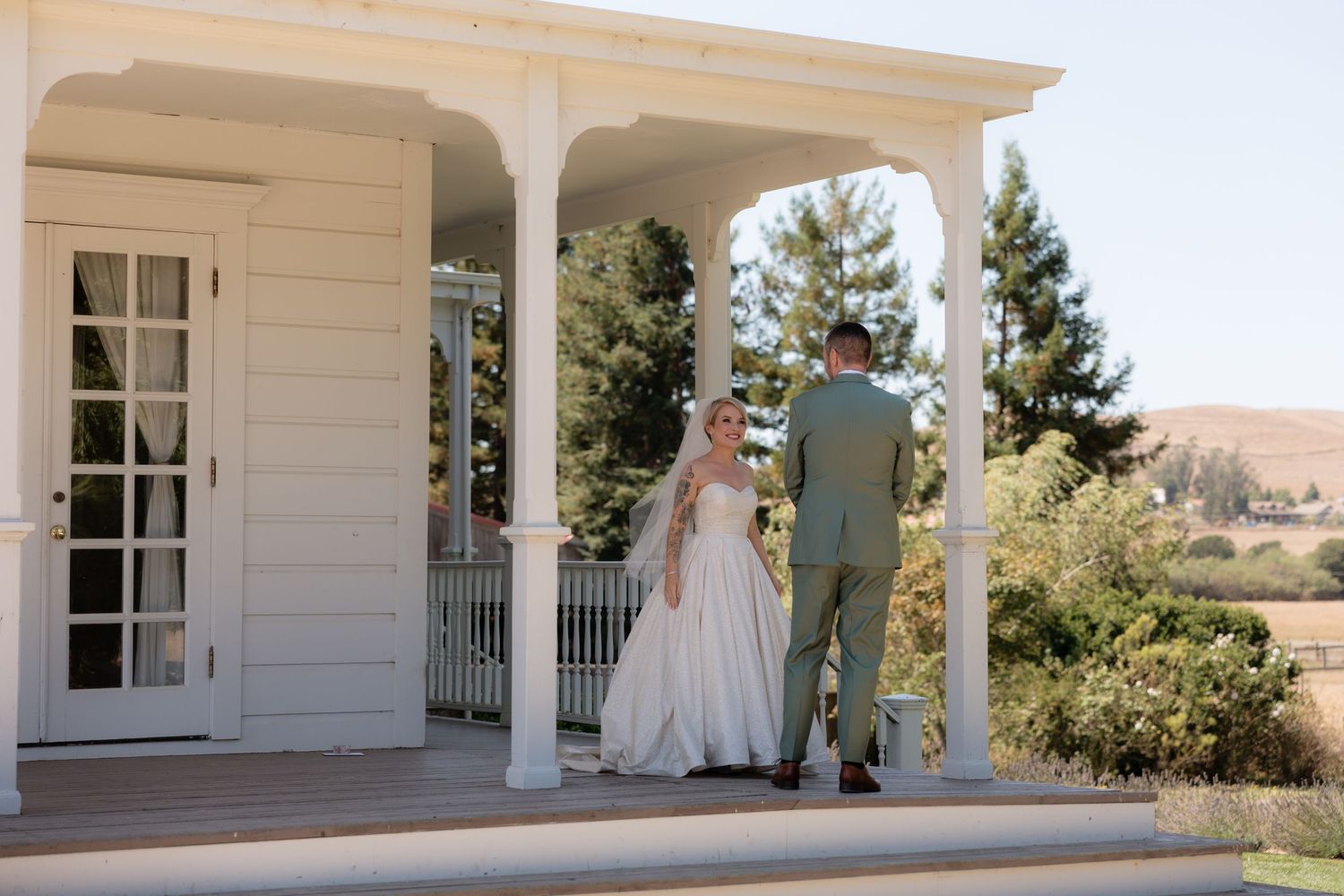 Bride and groom share a romantic first look on a white porch with scenic vineyard views on their wedding day.