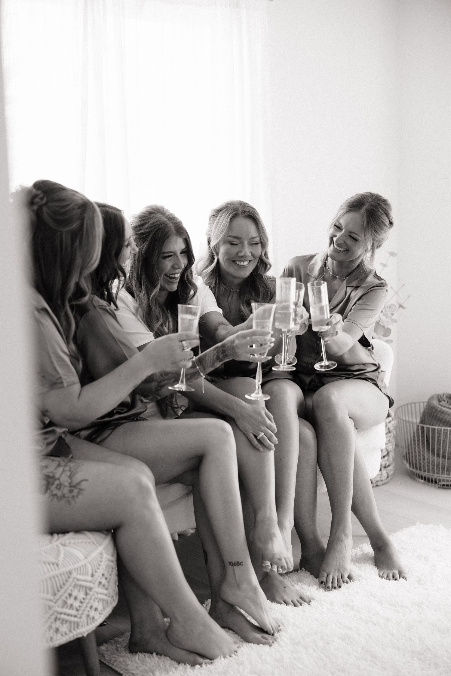 Bridesmaids in robes toasting with champagne glasses while sitting together in black and white photo.
