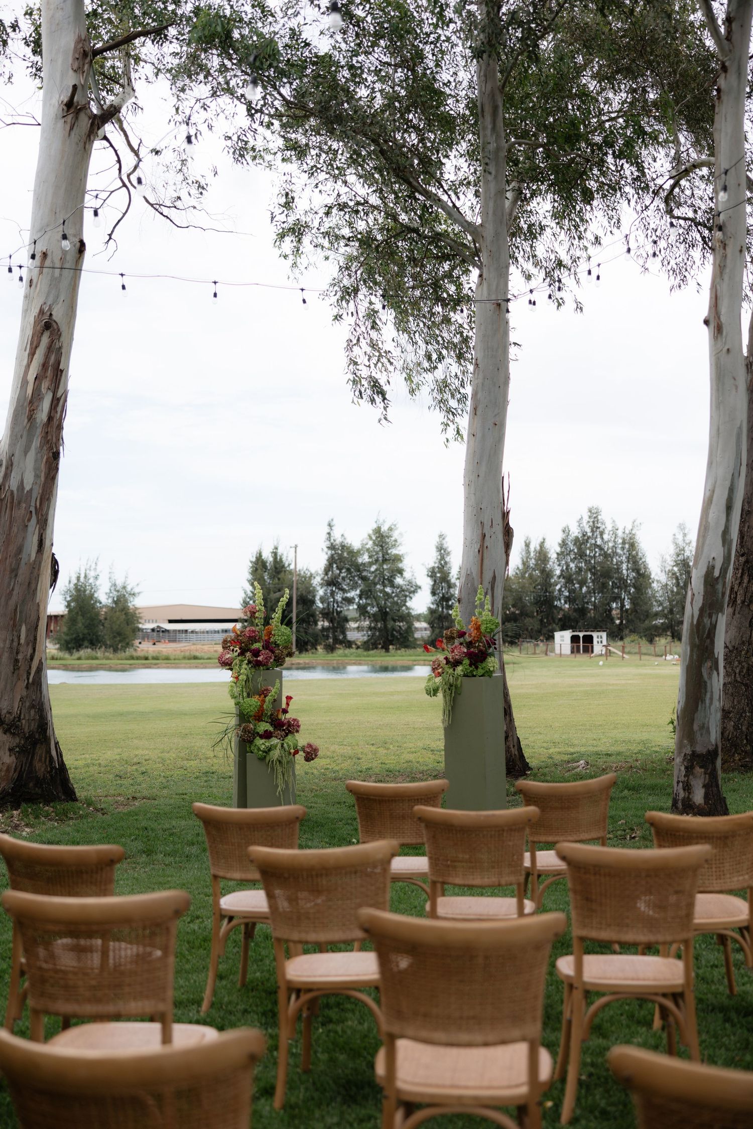 Outdoor wedding ceremony setup with wicker chairs, eucalyptus trees, and floral arrangements.