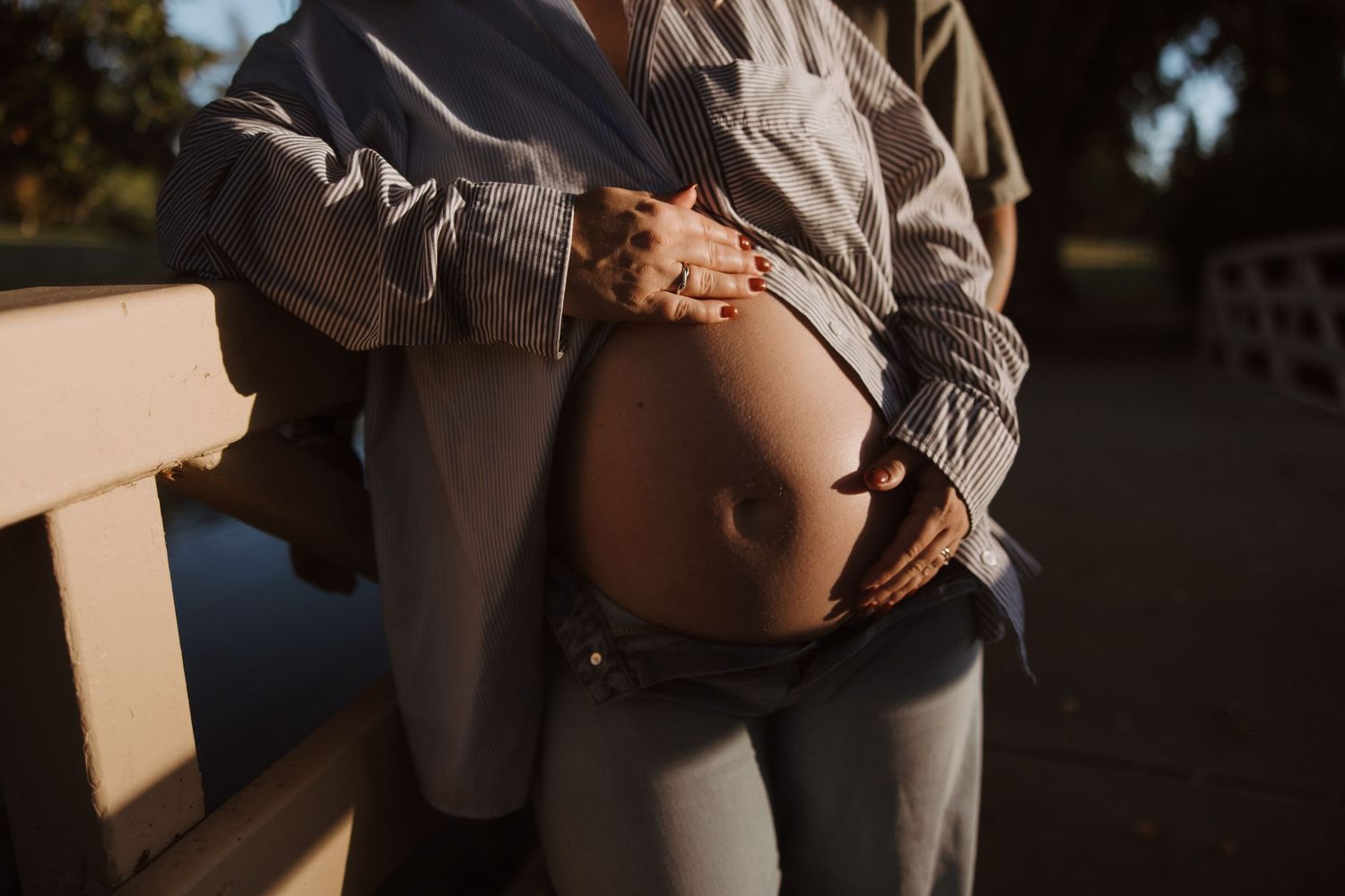 Close-up of a pregnant woman's belly with partner's hands gently cradling it outdoors.