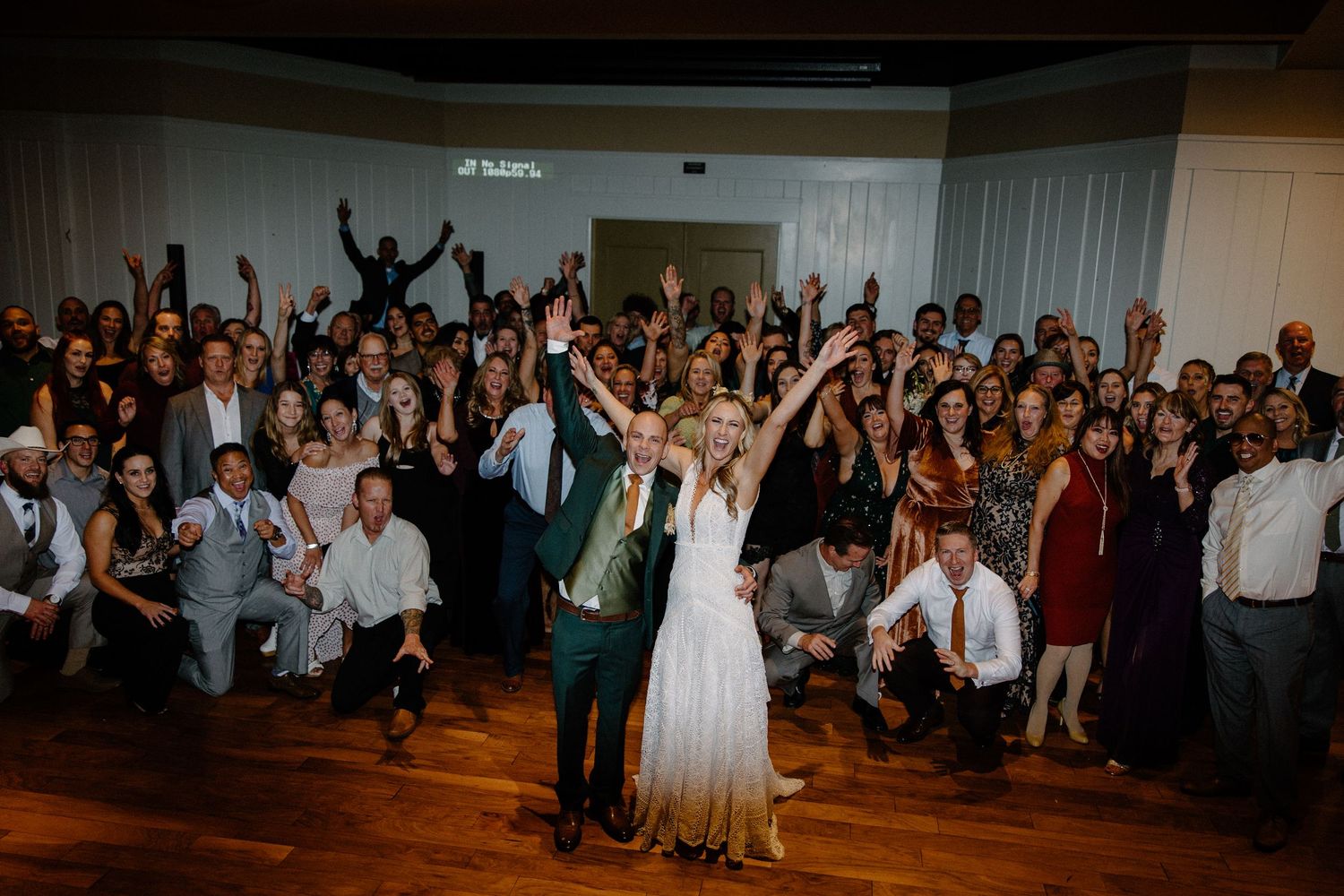 Bride and groom pose with large group of wedding guests on dance floor at reception finale.