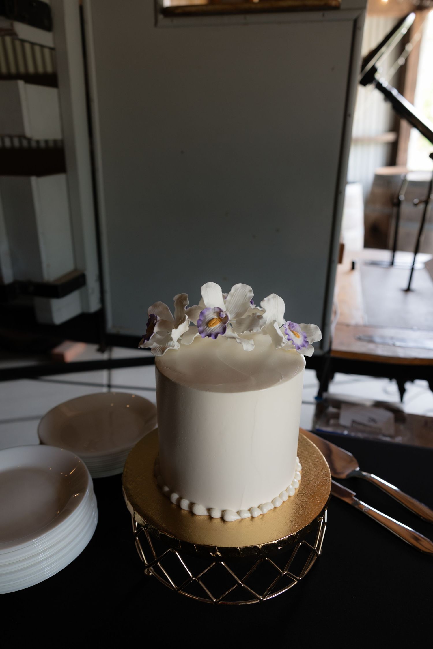 Elegant white single-tier wedding cake with floral topper on gold stand.