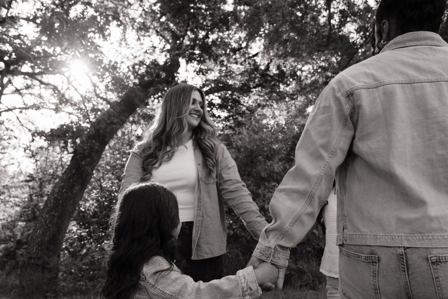 Black and white family photo holding hands under sunlit trees outdoors.