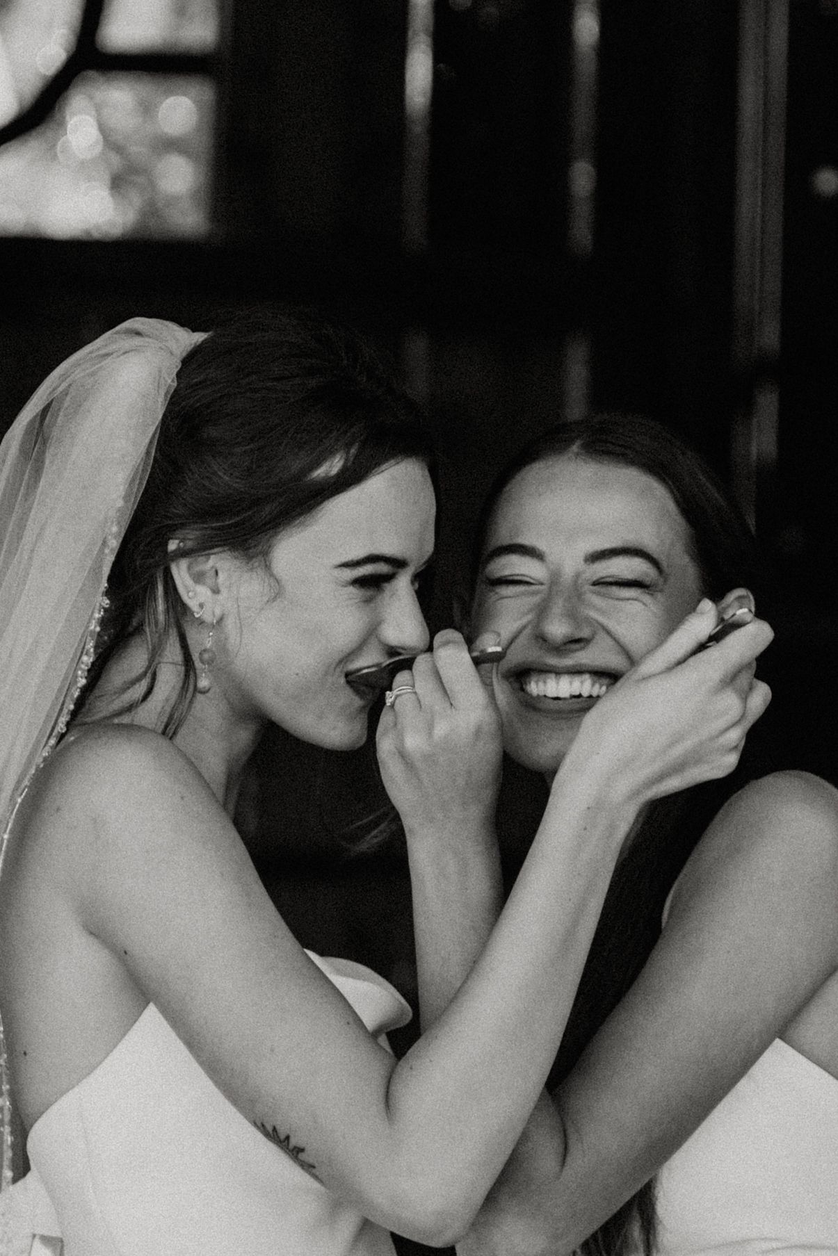 Two brides laughing joyfully together in a black and white wedding photo full of genuine emotion.