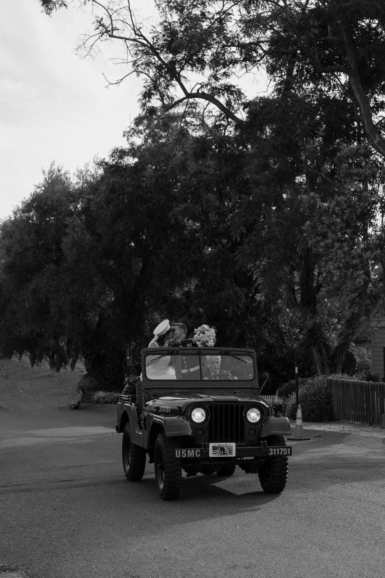 Black and white photo of newlyweds riding in vintage USMC Jeep after wedding ceremony.
