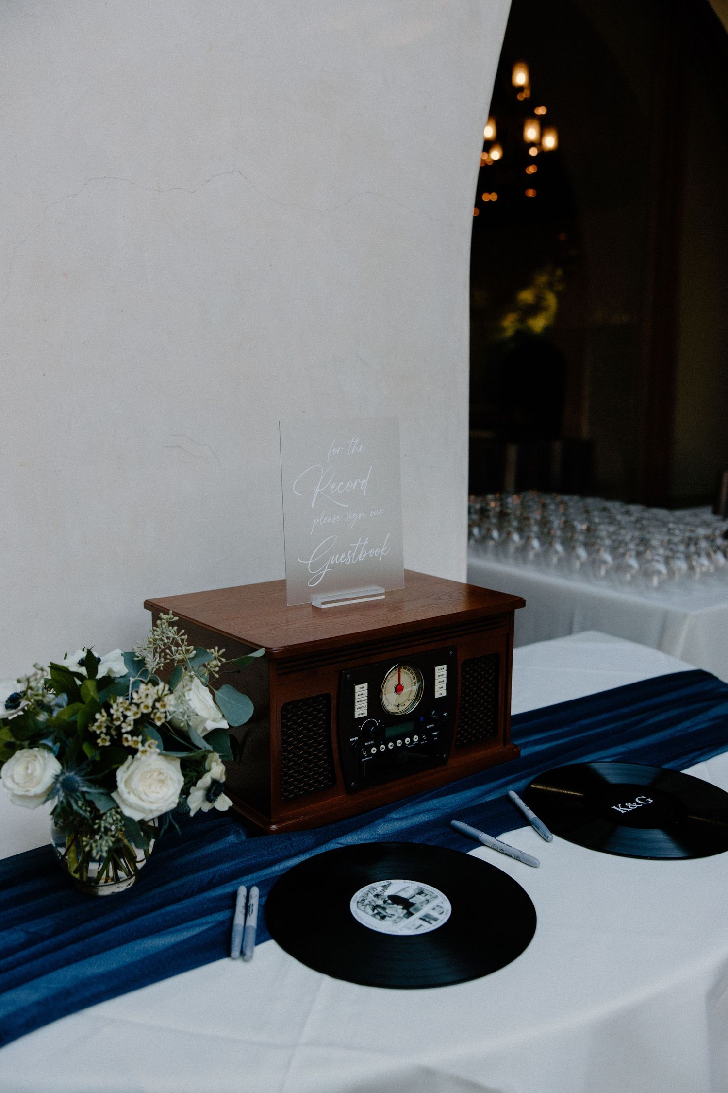 Elegant wedding guest book table featuring a vintage record player, vinyl records, and white floral arrangement.