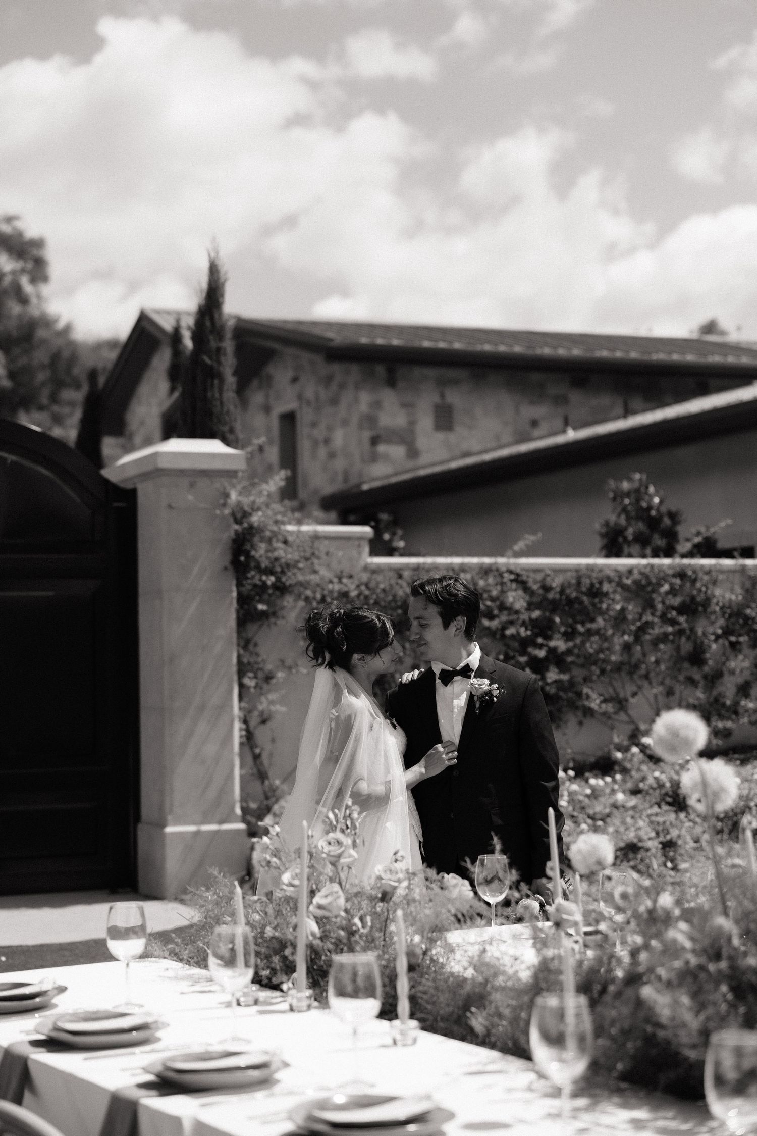 Bride and groom share a romantic moment beside an outdoor wedding reception table at a vineyard.