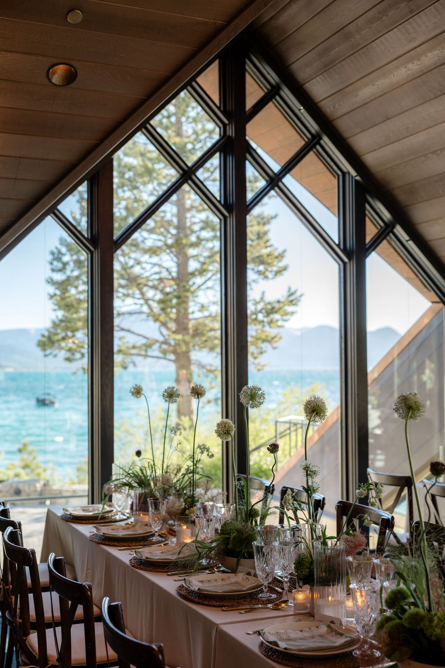 Elegant wedding reception table with floral centerpieces beside floor-to-ceiling triangular windows overlooking Lake Tahoe.
