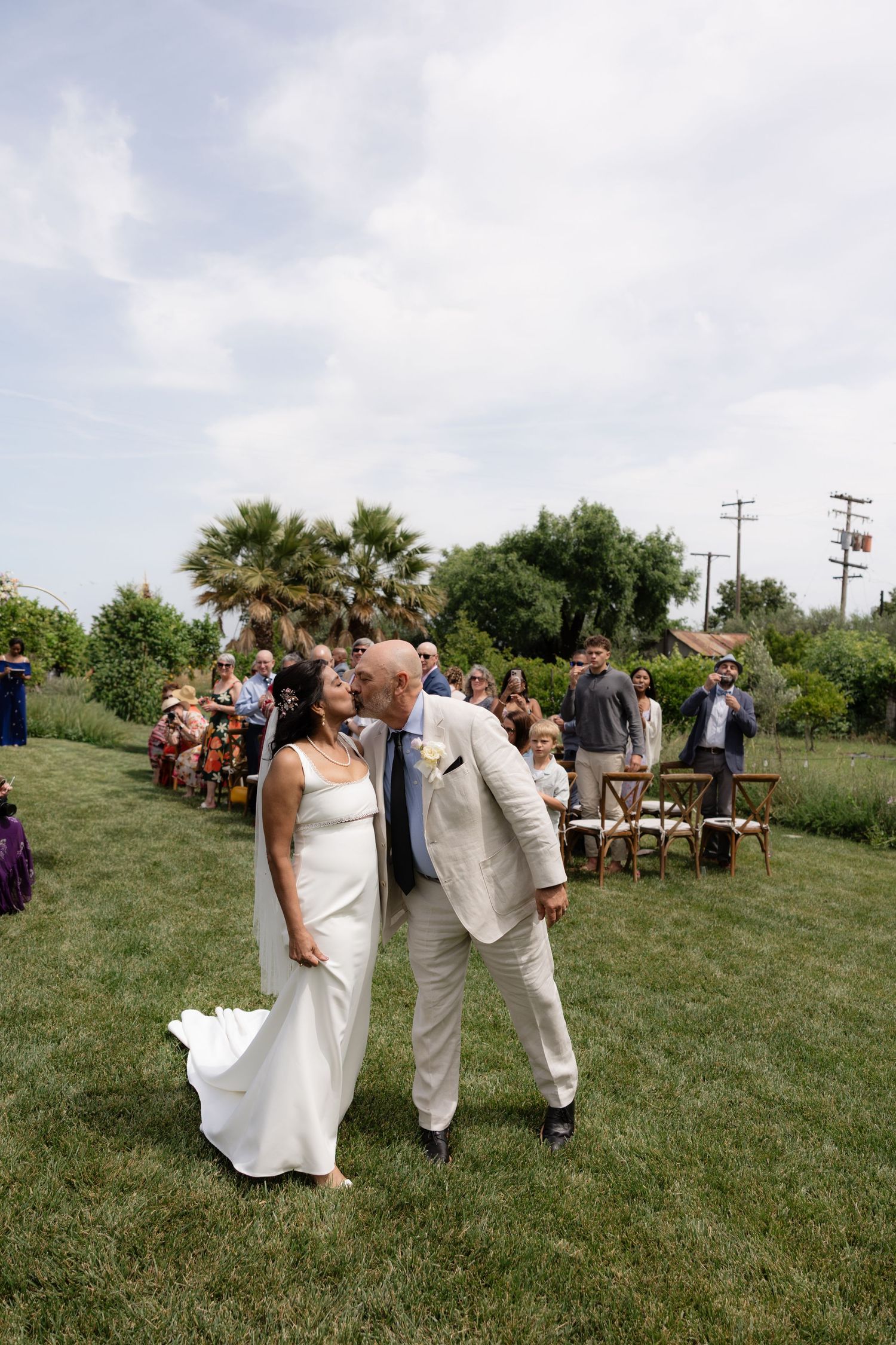 Newlywed couple shares a kiss while walking down the aisle at their outdoor garden wedding.