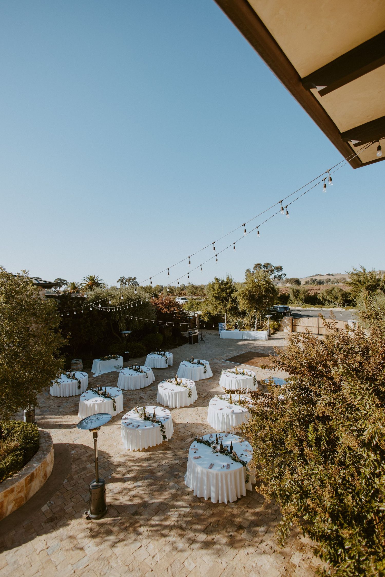 Elegant outdoor wedding reception with white draped tables and string lights at vineyard venue.