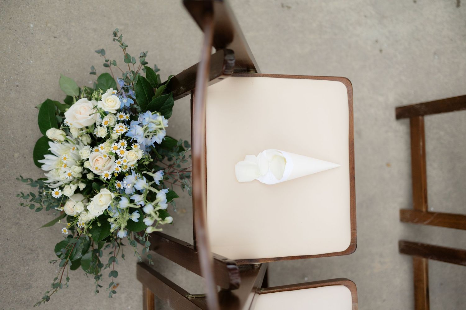 Blue and white floral bouquet resting on a wooden folding chair at an elegant wedding ceremony.