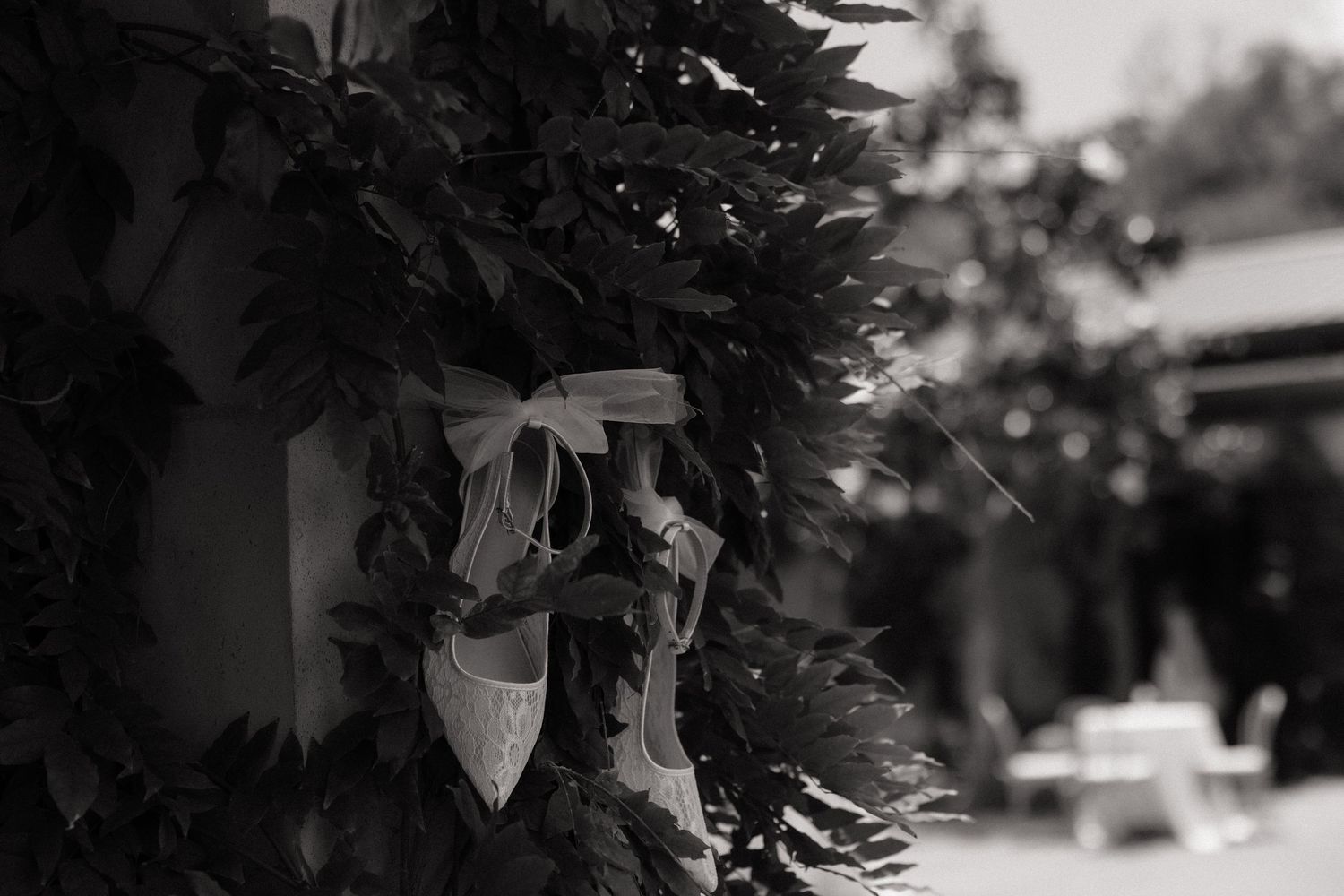 Delicate white bridal shoes tied with a ribbon hanging on a lush green floral wreath.