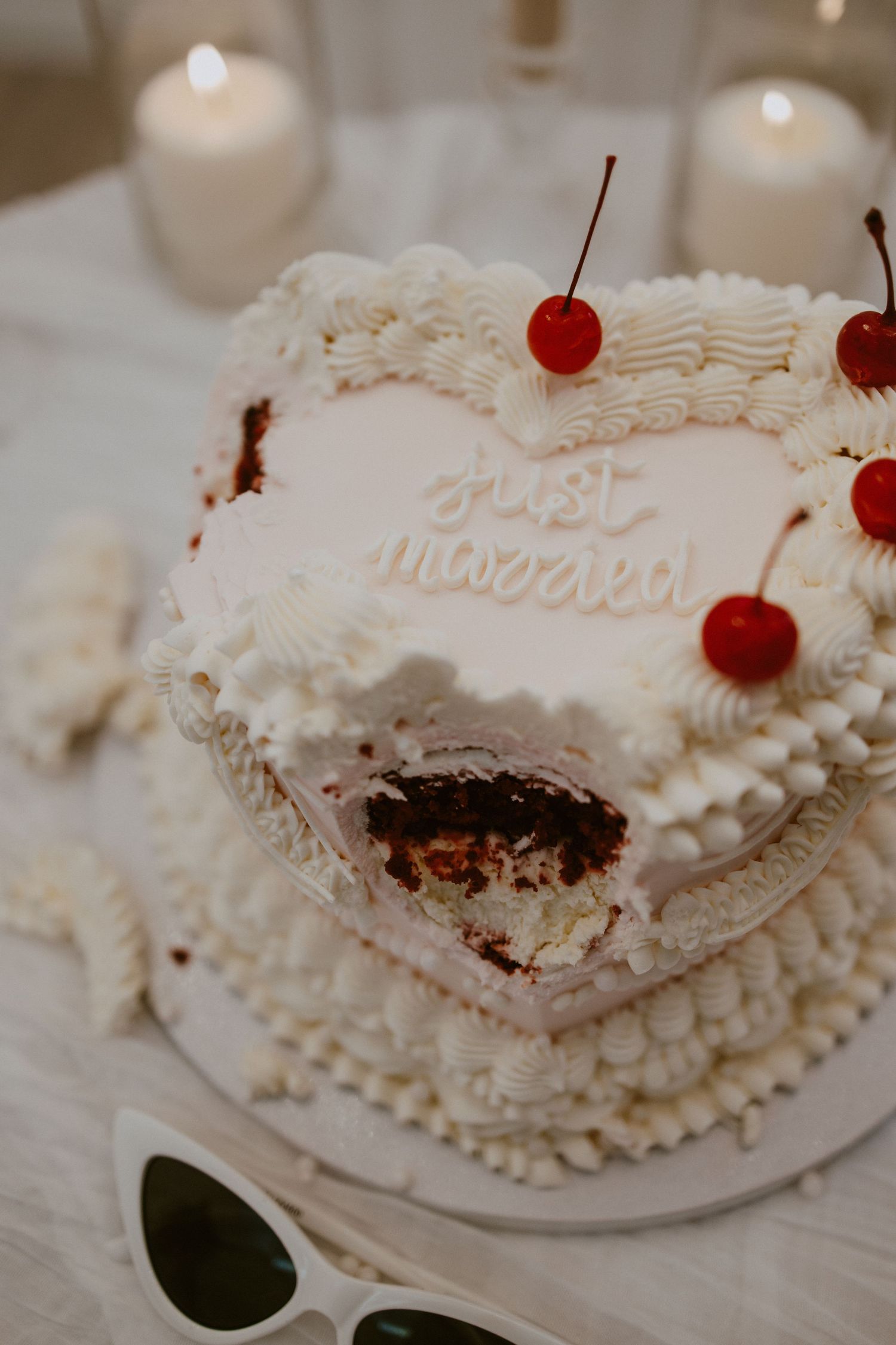 Heart-shaped just married wedding cake with cherries and chocolate interior on a white table.