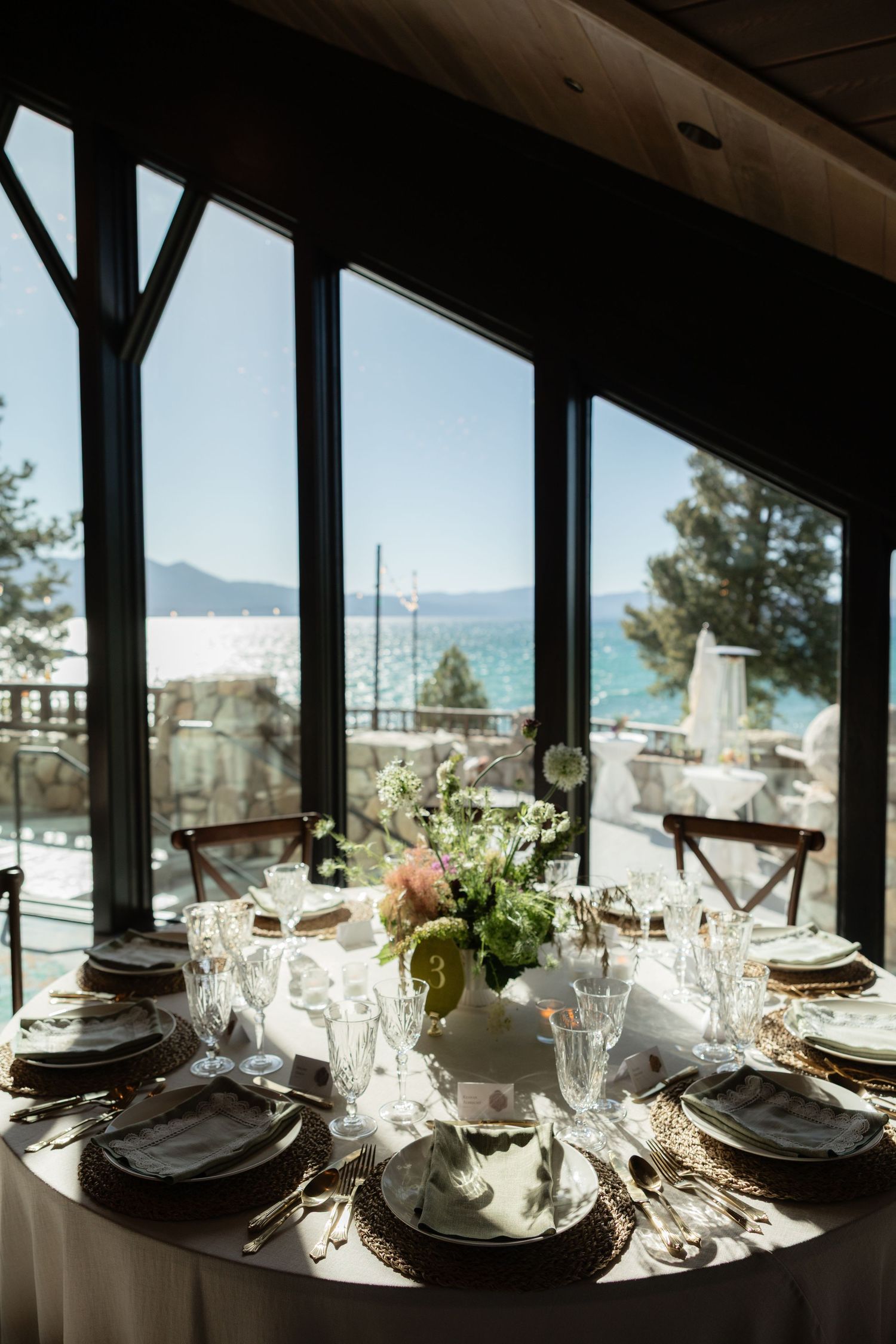Elegant wedding reception table set with florals and glassware overlooking a stunning lakeside view.