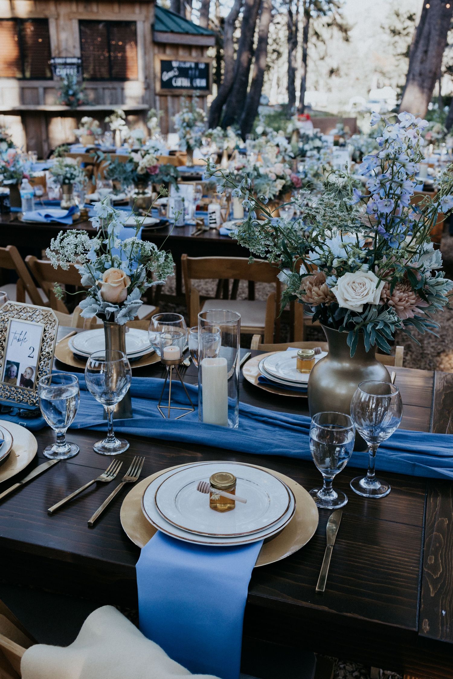 Elegant outdoor wedding reception tablescape with blue runners, white roses, and gold accents.