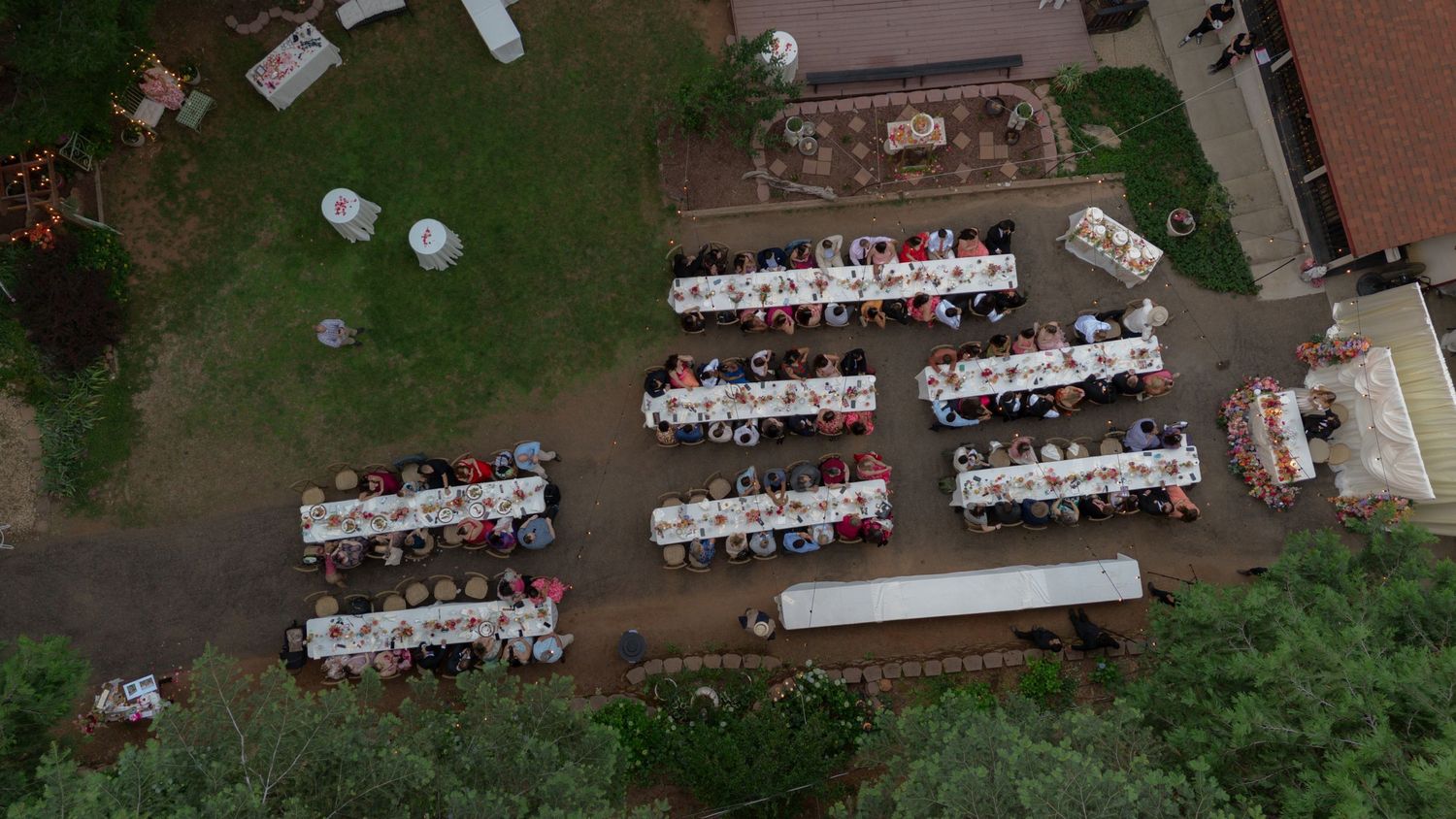 Aerial view of an outdoor banquet with long tables and guests seated in a garden setting.