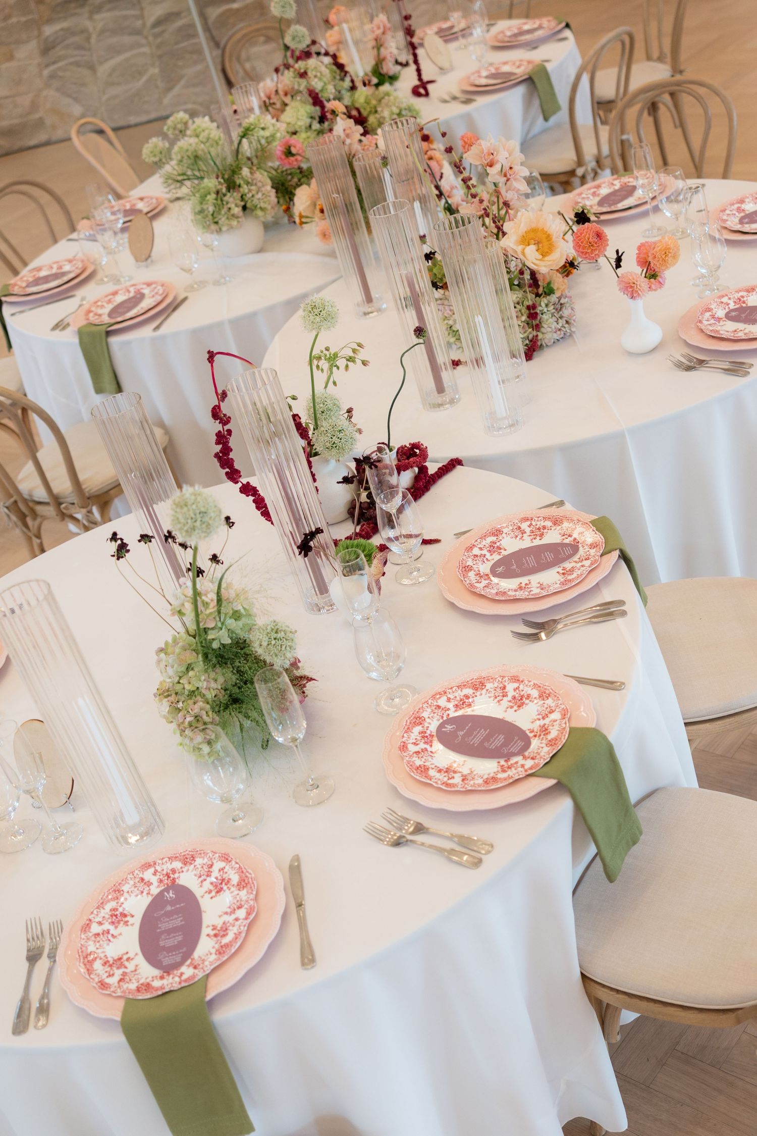 Elegant wedding reception table set with pink floral plates, green napkins, and fresh flower centerpieces.