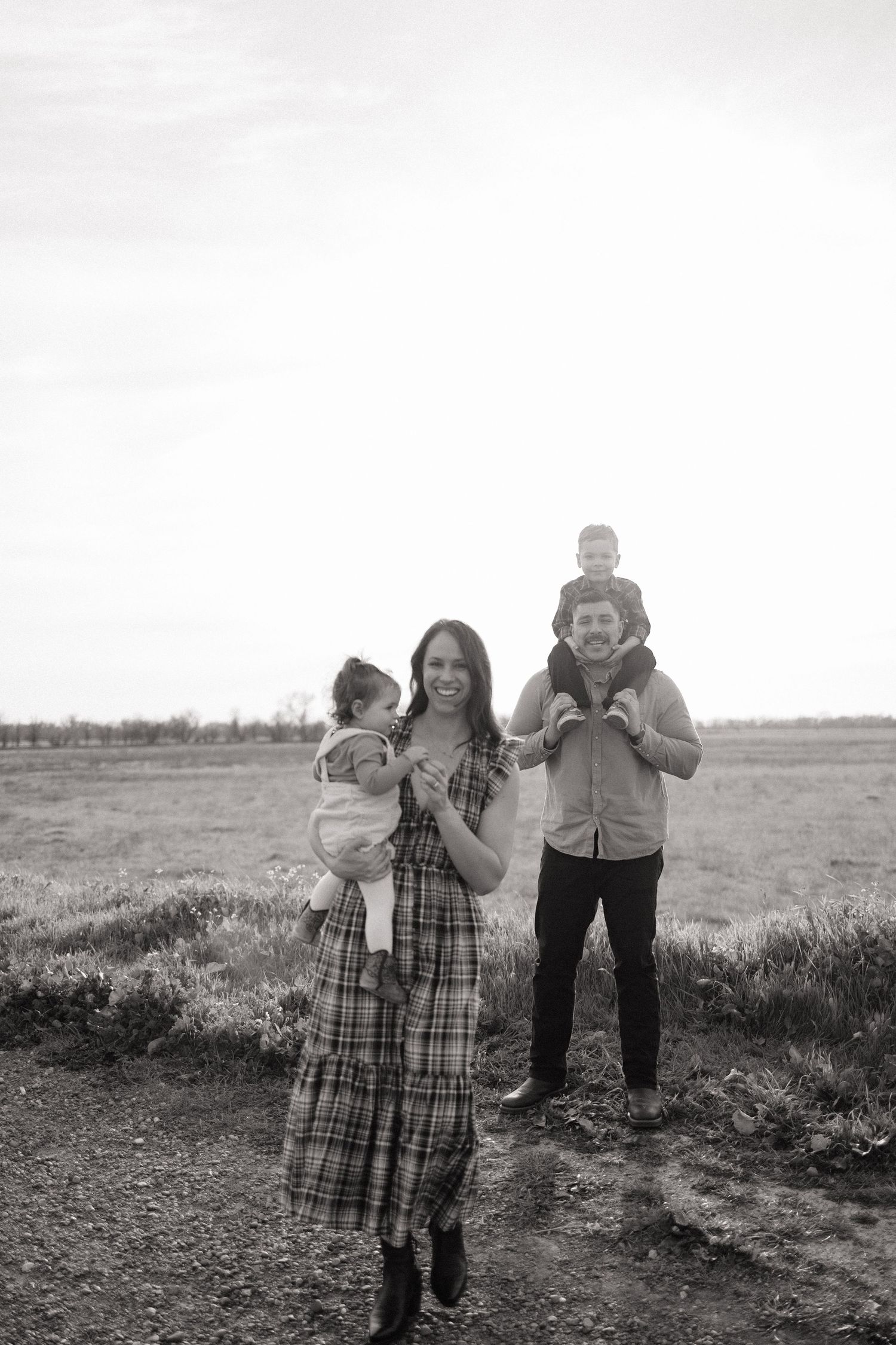 Black and white portrait of a smiling family of four in an open field.