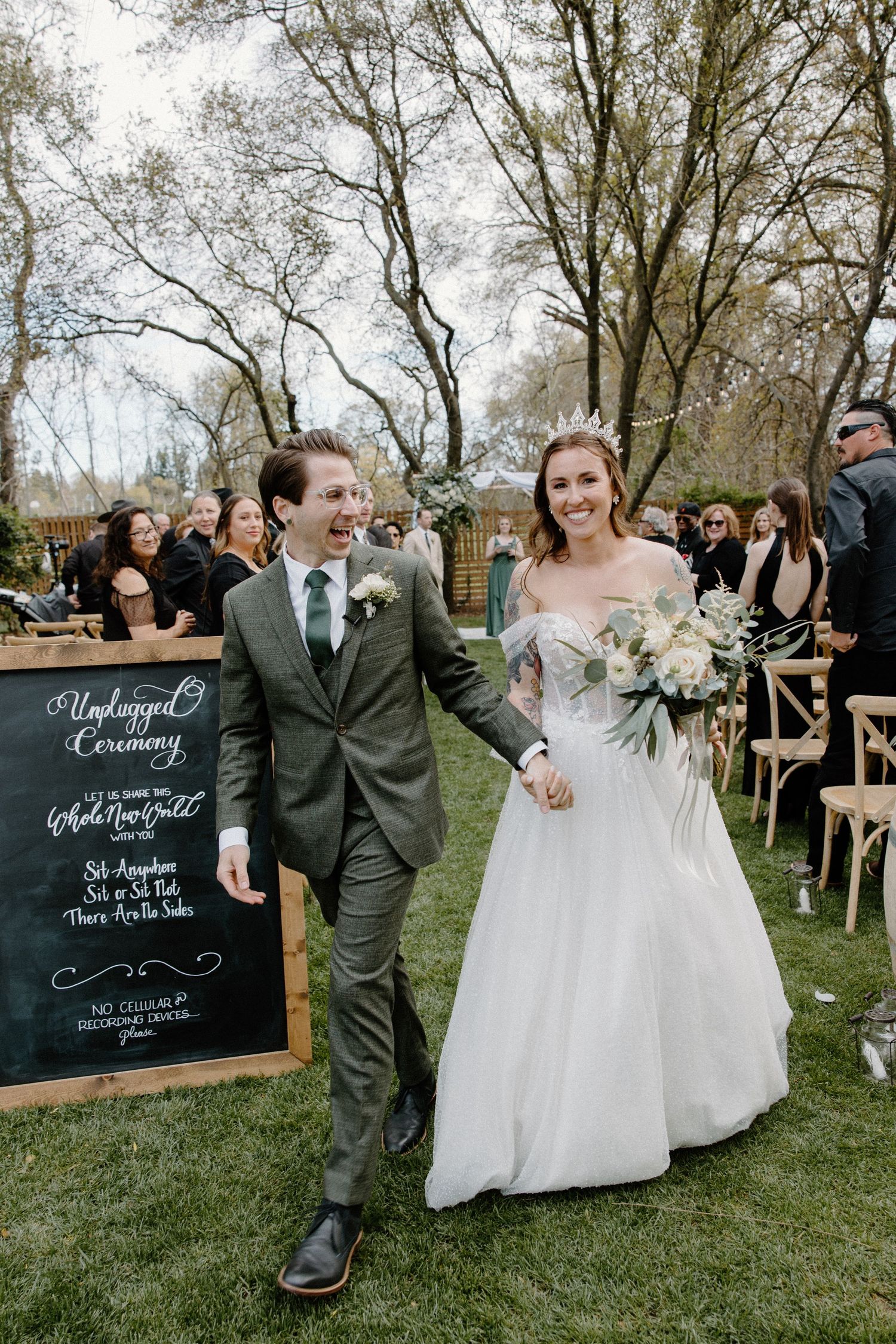 Smiling bride and groom walk back down aisle at outdoor garden wedding ceremony.