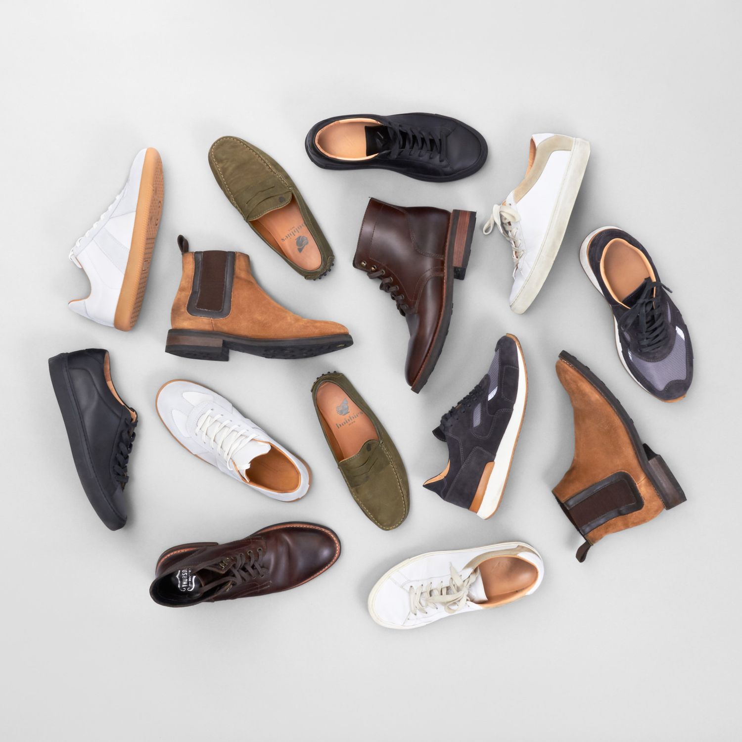 Flat lay of diverse shoe styles including boots, sneakers, and oxfords in neutral earth tones.