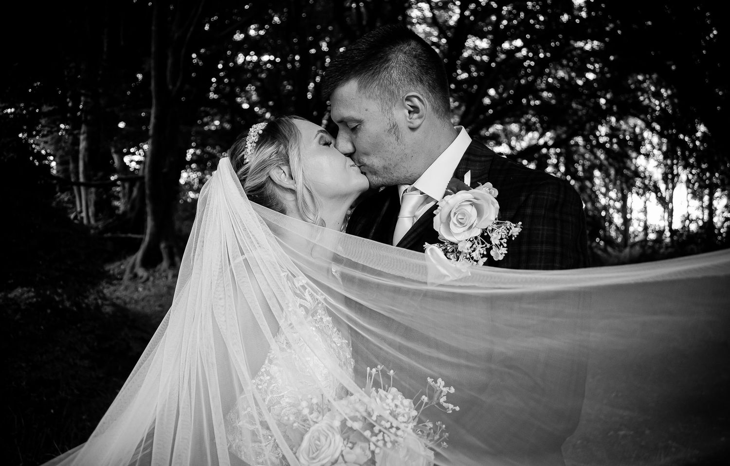Black-and-white close-up of a newlywed couple kissing beneath the bride’s veil