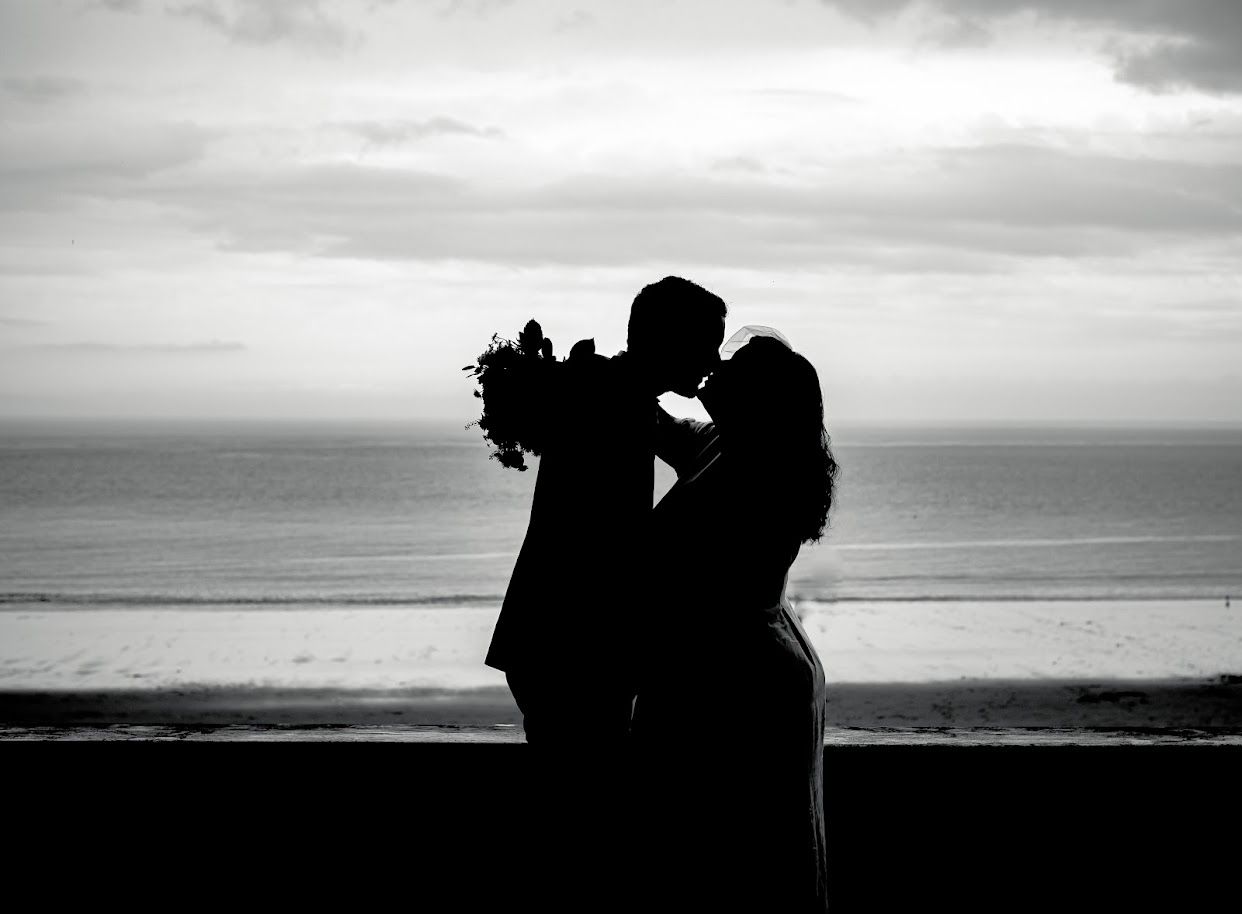 Black-and-white silhouette of a newlywed couple kissing beside the sea at Barry Island