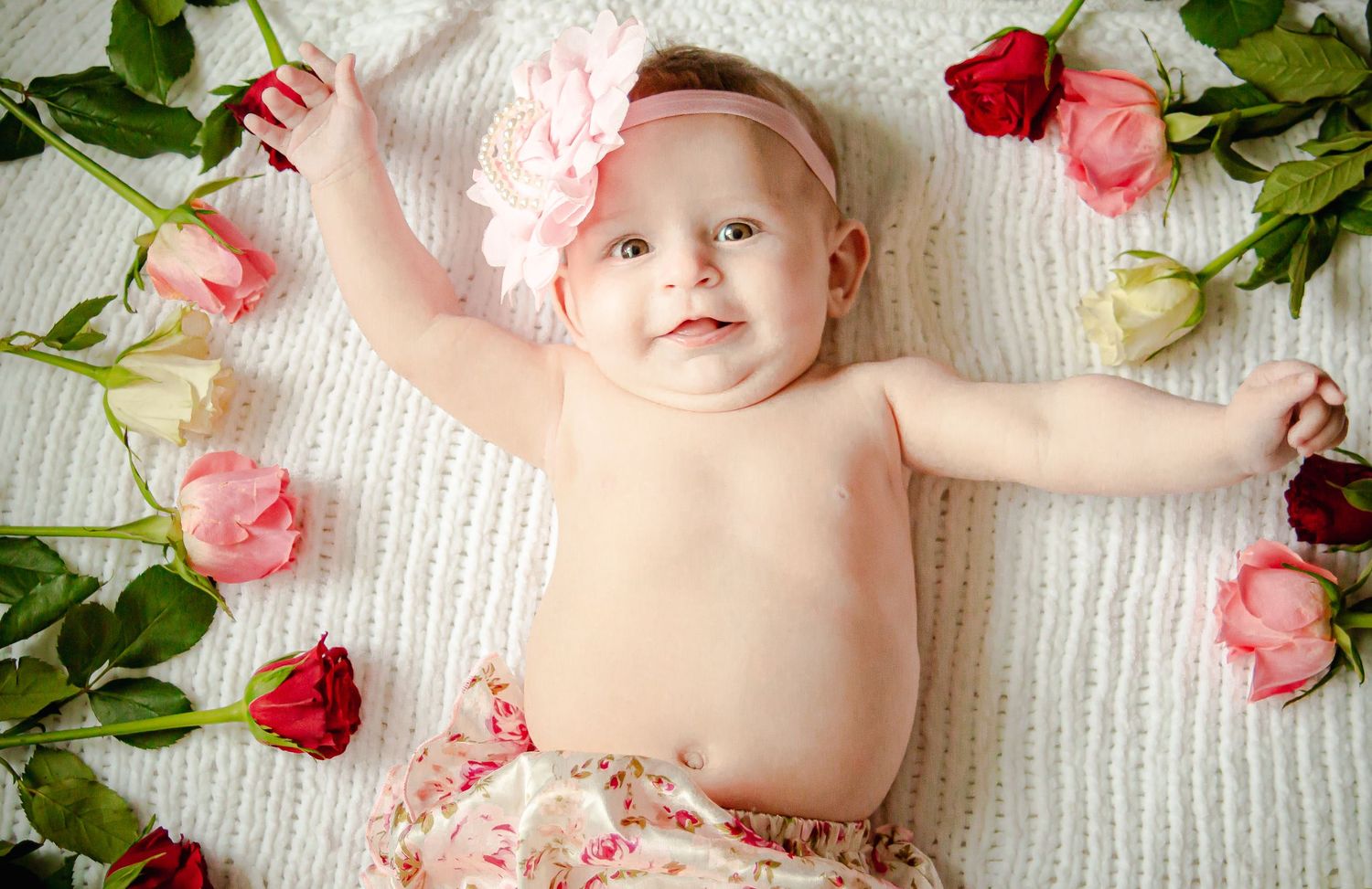 Smiling baby girl lying among pink and red roses