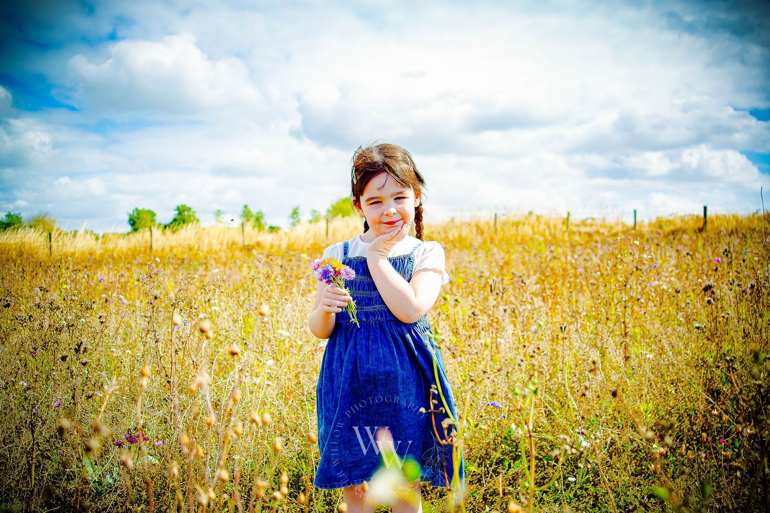Young girl standing among wildflowers beneath a dramatic summer sky
