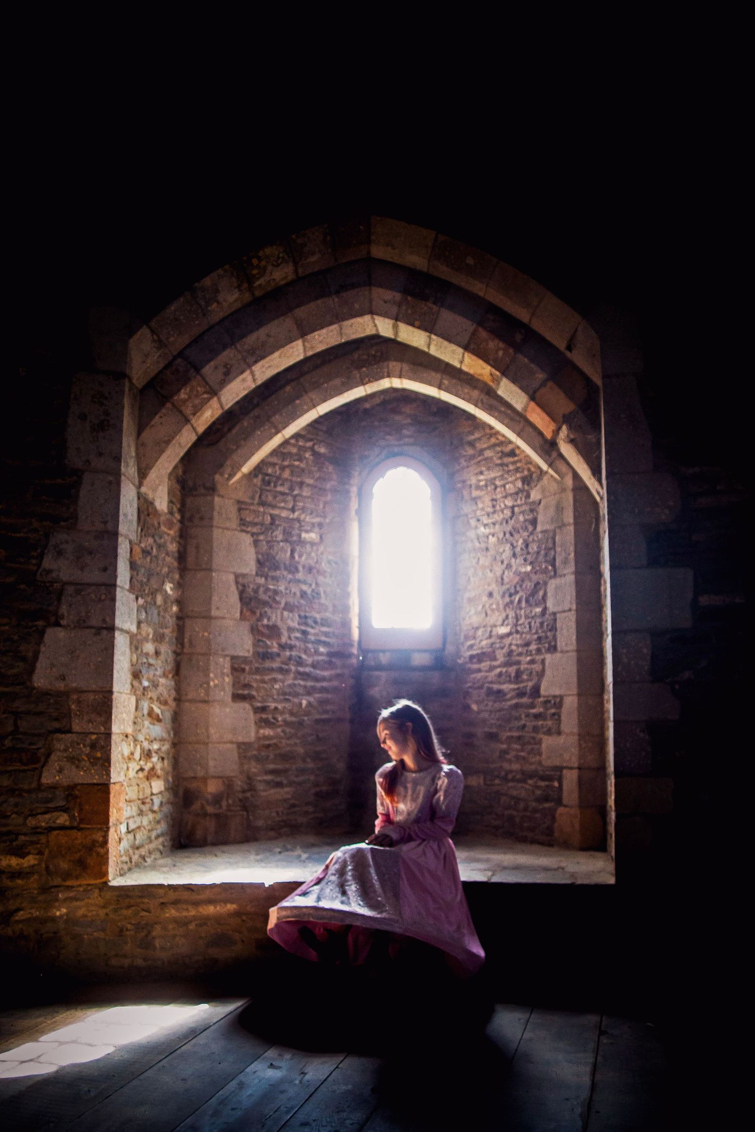 Child in a pink princess dress sitting inside a tall castle window