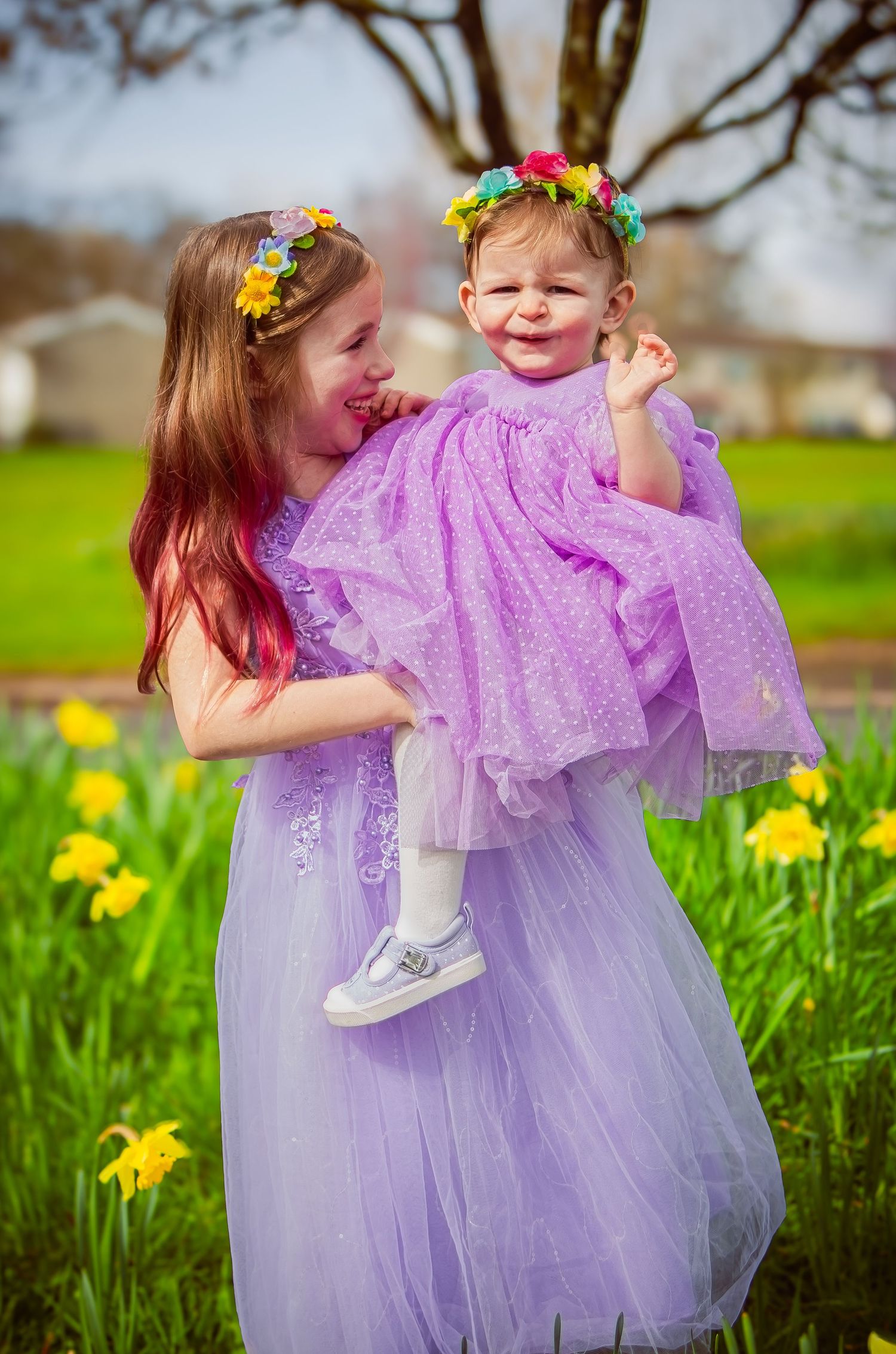Two sisters smiling at each other among yellow daffodils