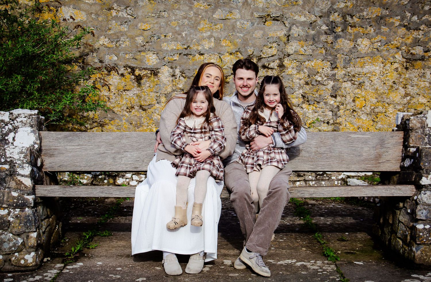 Parents and their daughters smiling together on a rustic bench