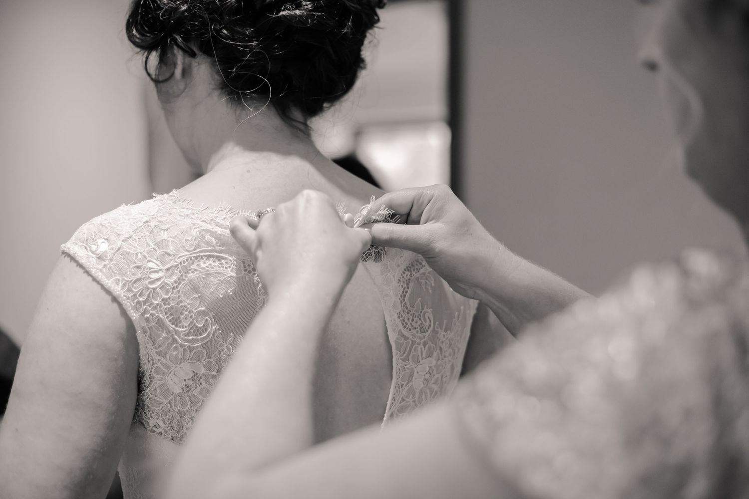 Bridesmaid fastening the back of the bride’s lace wedding dress