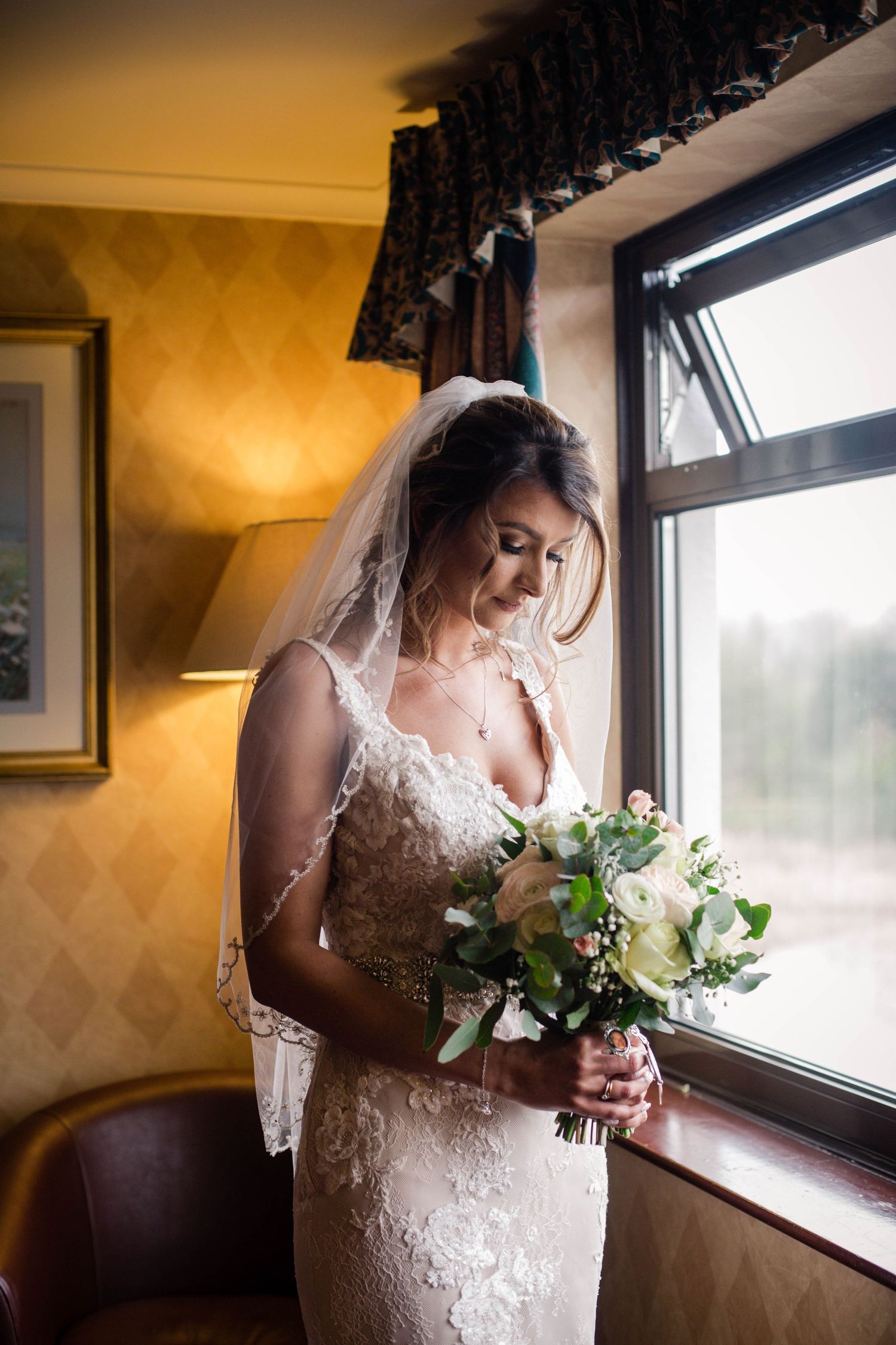 Bride holding her pastel bouquet beside a window at Pencoed House