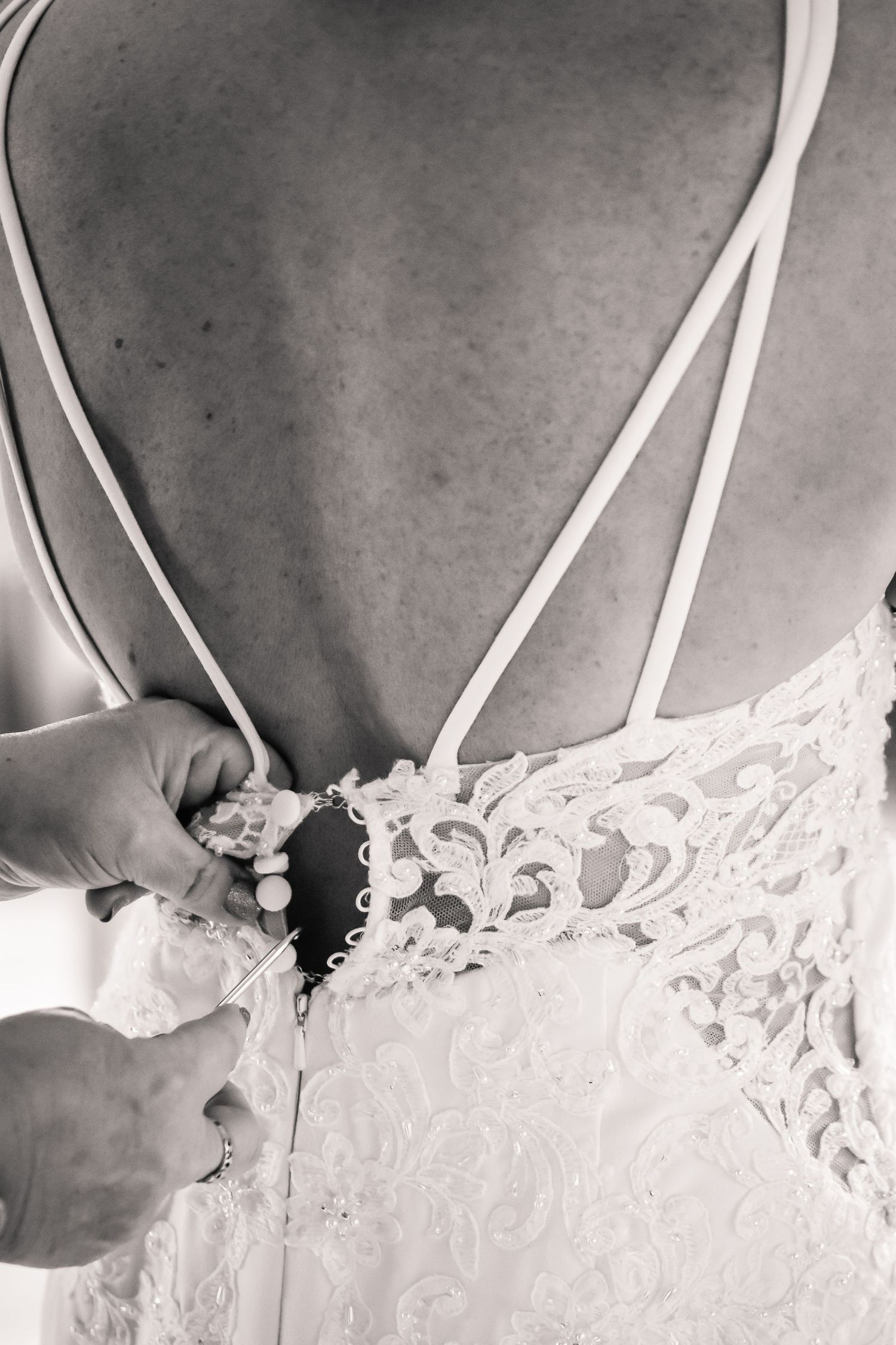 Black and white close-up of a lace wedding dress being fastened