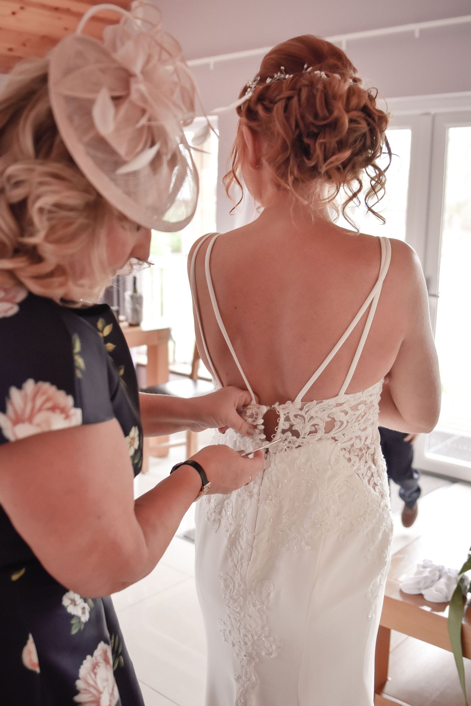 Mother of bride fastening the back of the bride’s lace wedding dress